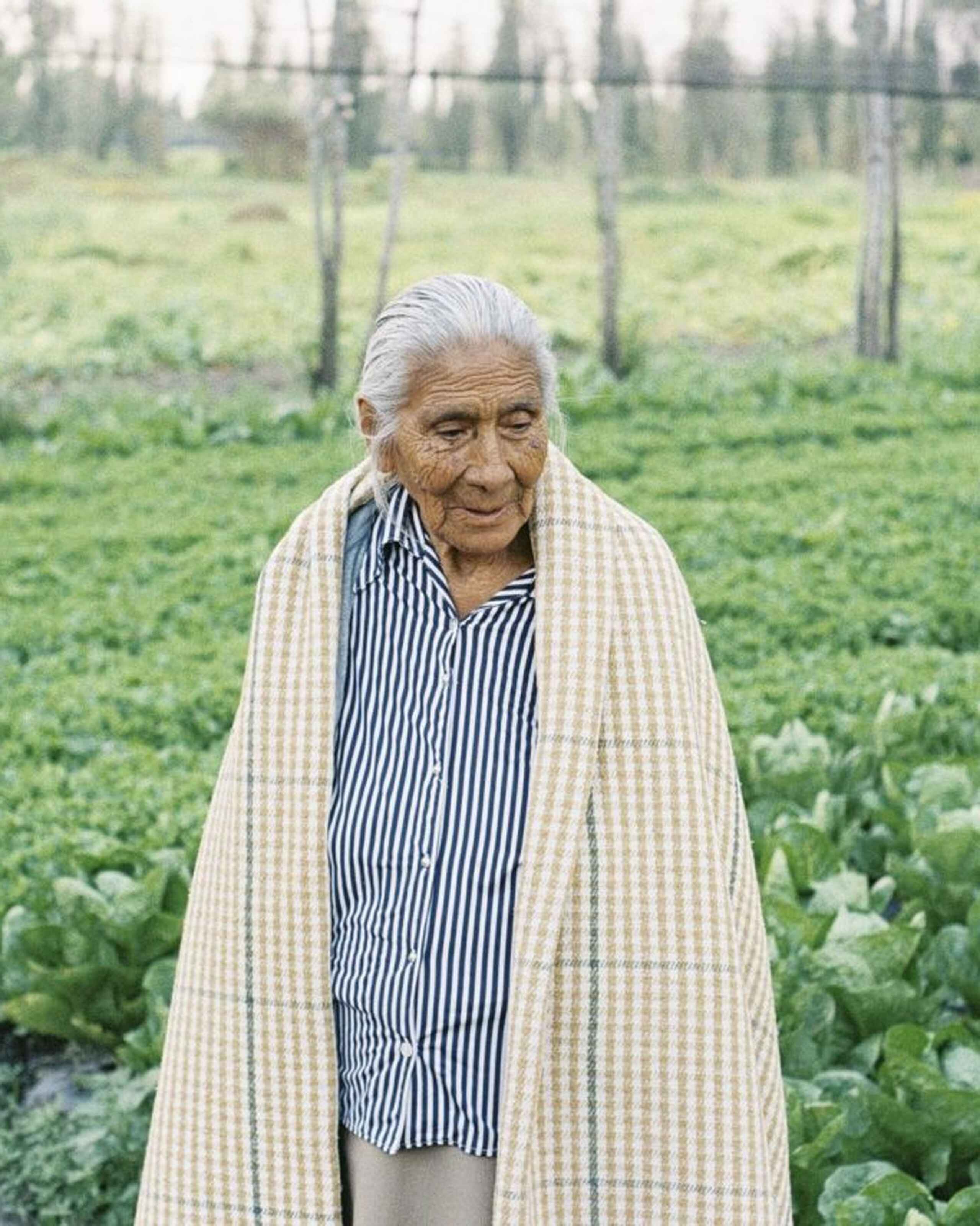 Elderly woman standing in a vegetable garden wearing a striped shirt and woven shawl