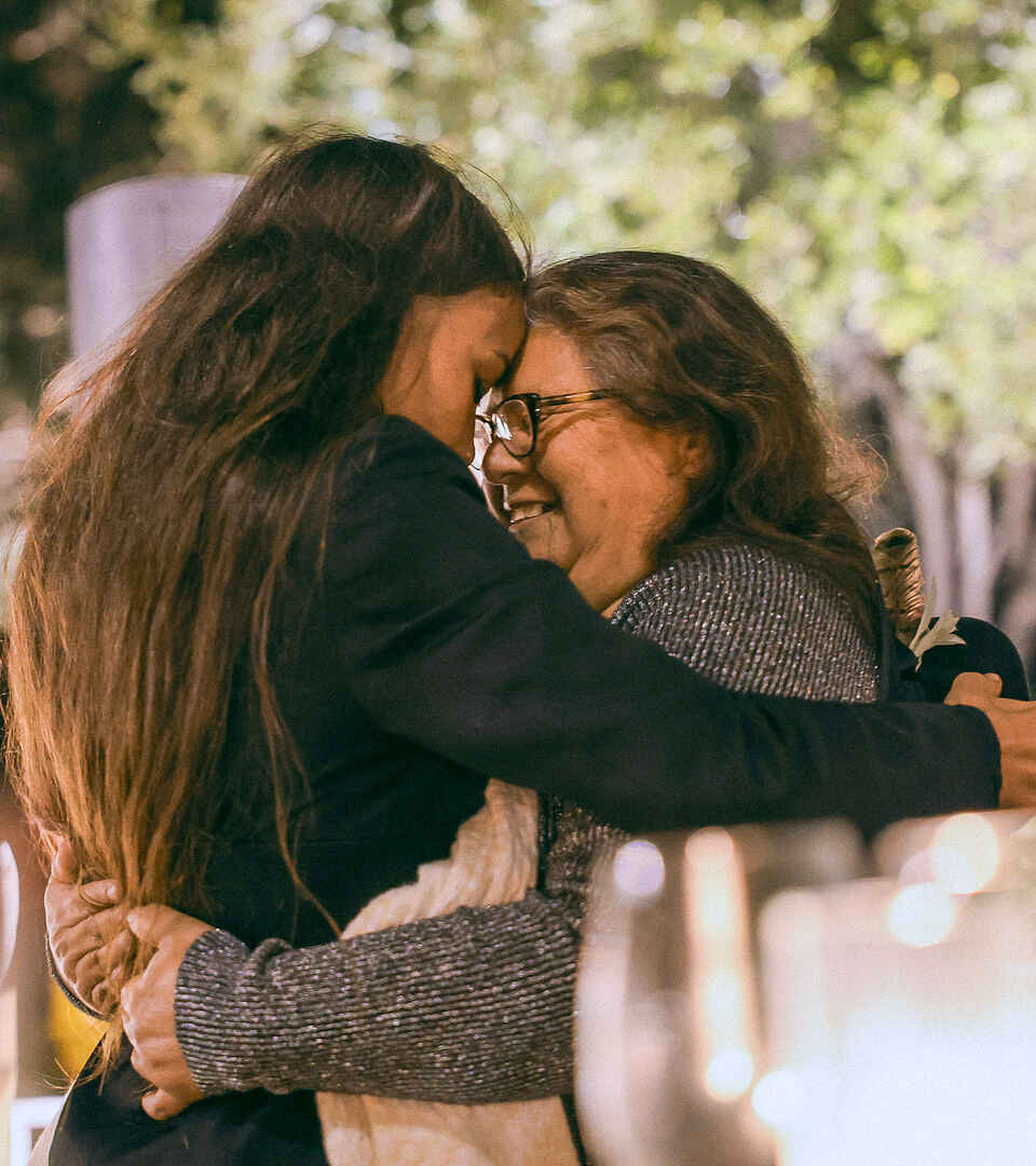 Two women embracing outdoors under blooming trees at night