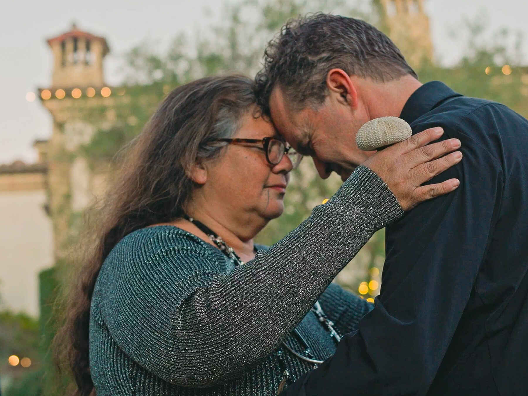 A man and woman embrace and share a tender moment outdoors in front of an ornate castle