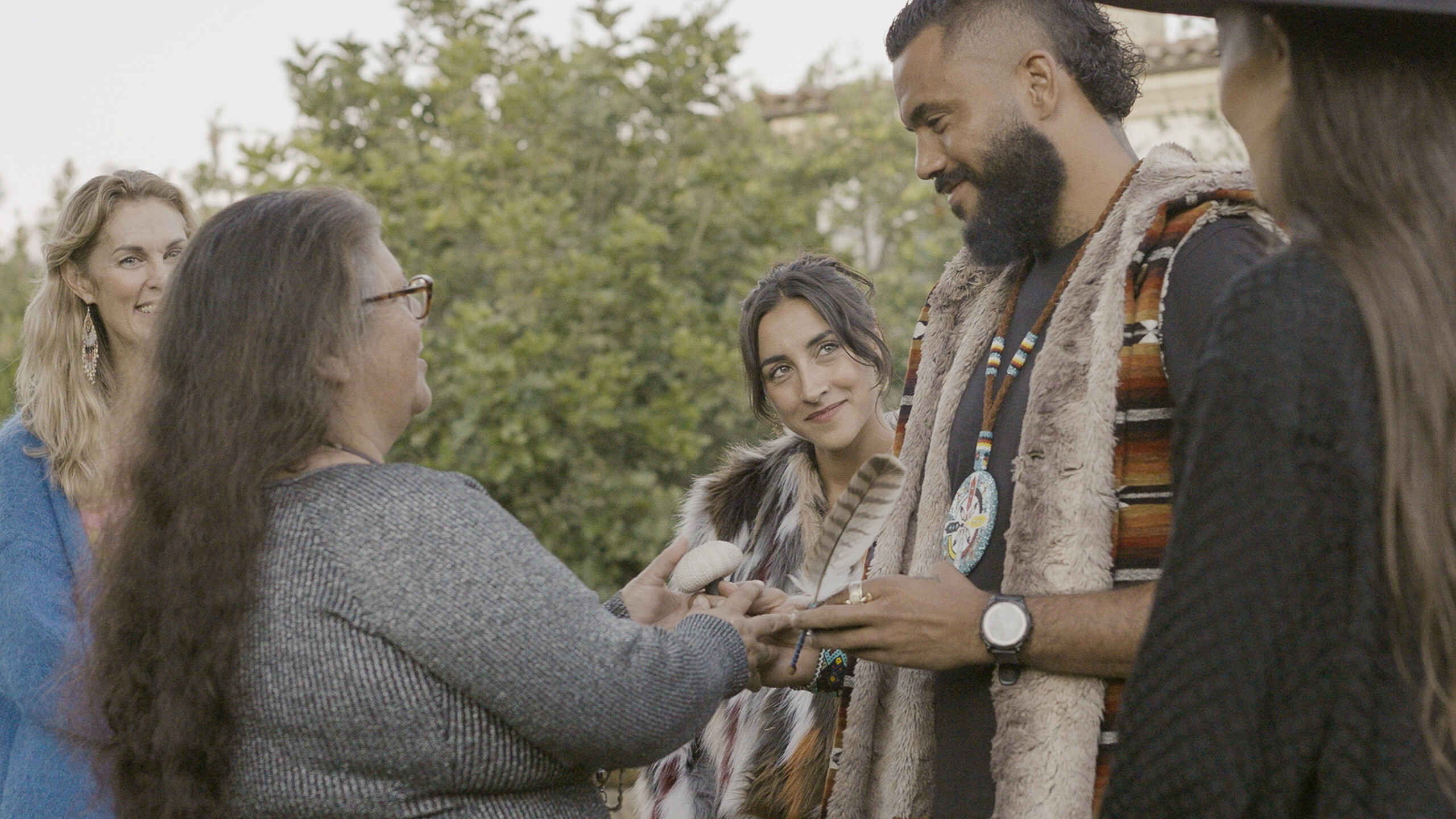 Indigenous man and woman sharing traditional knowledge with community members outdoors