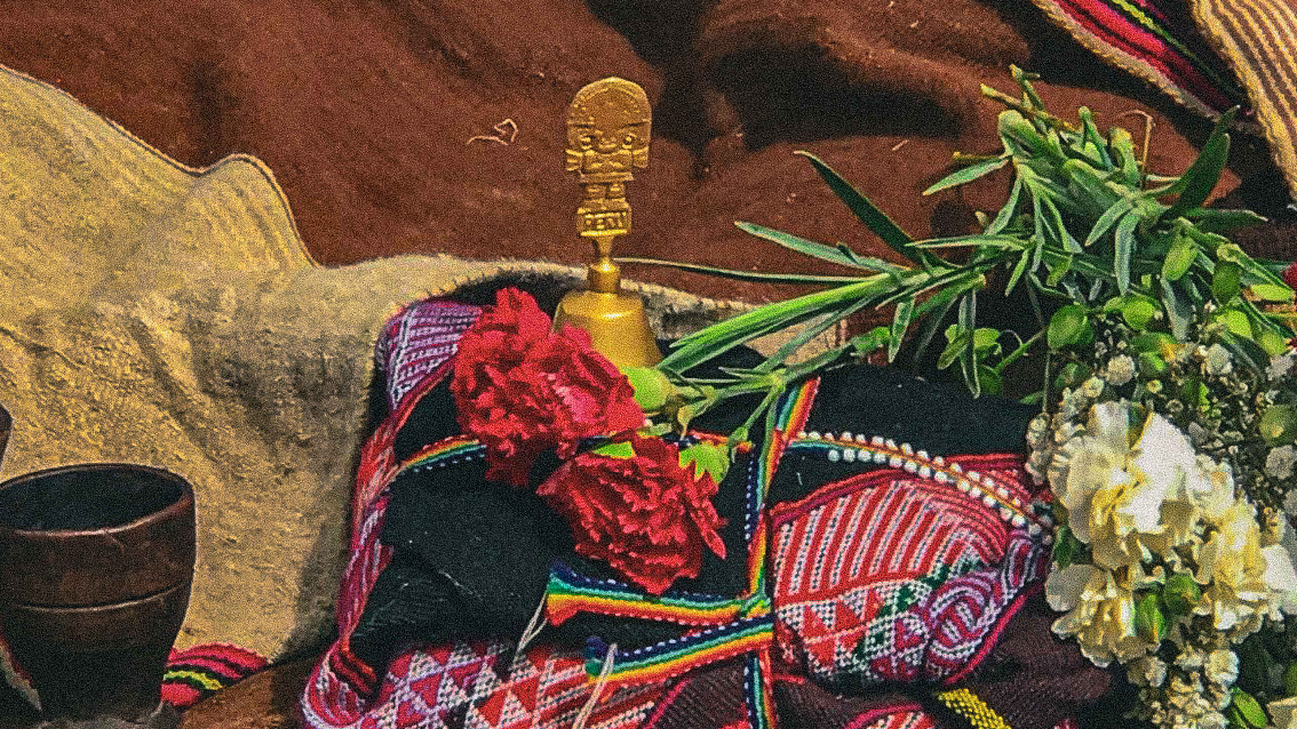 Traditional woven textile with red carnations and white flowers arranged ceremonially with a golden staff
