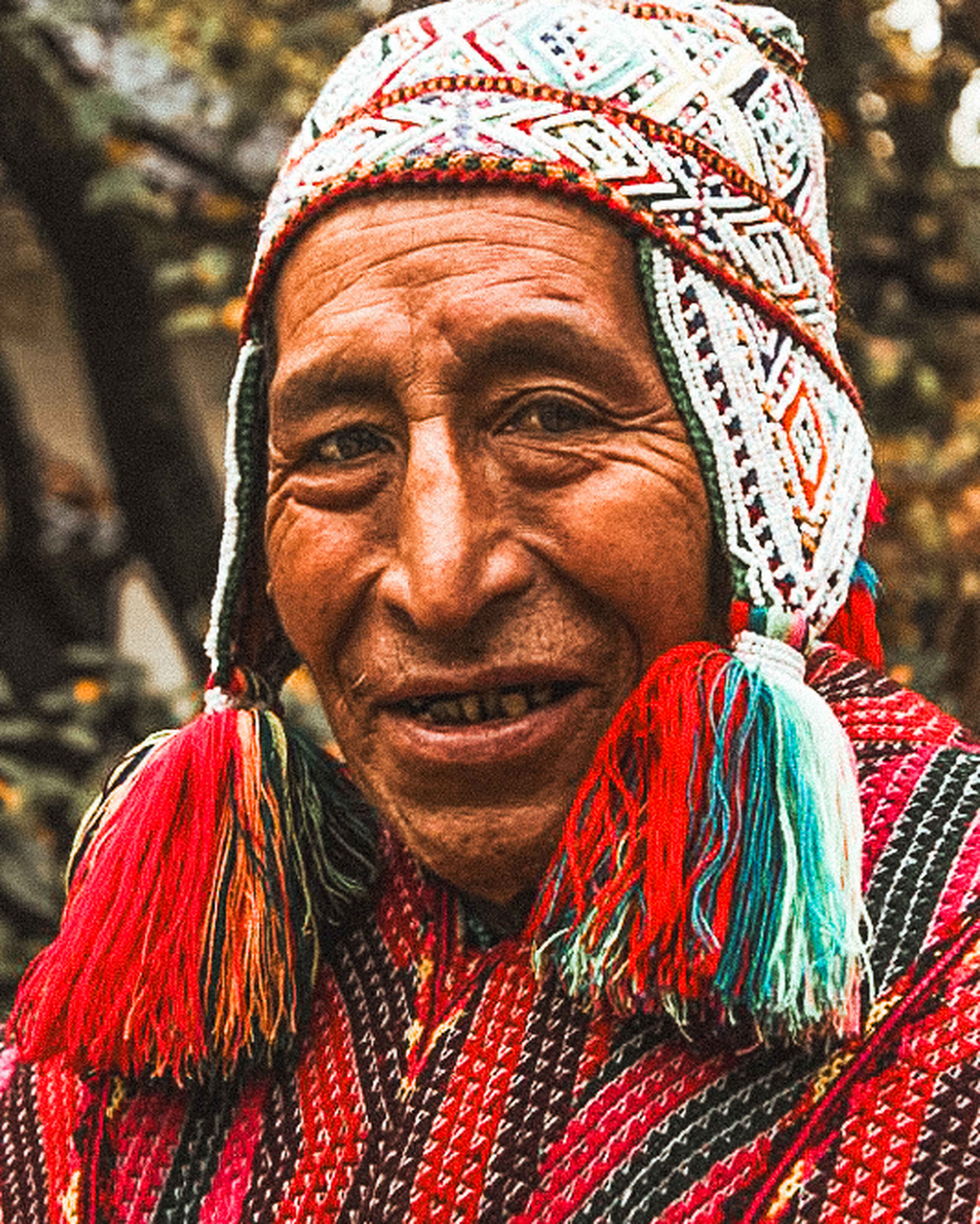 Don Sebastian Sucli, an elder wearing traditional Andean textiles and a woven head covering, smiles at the camera