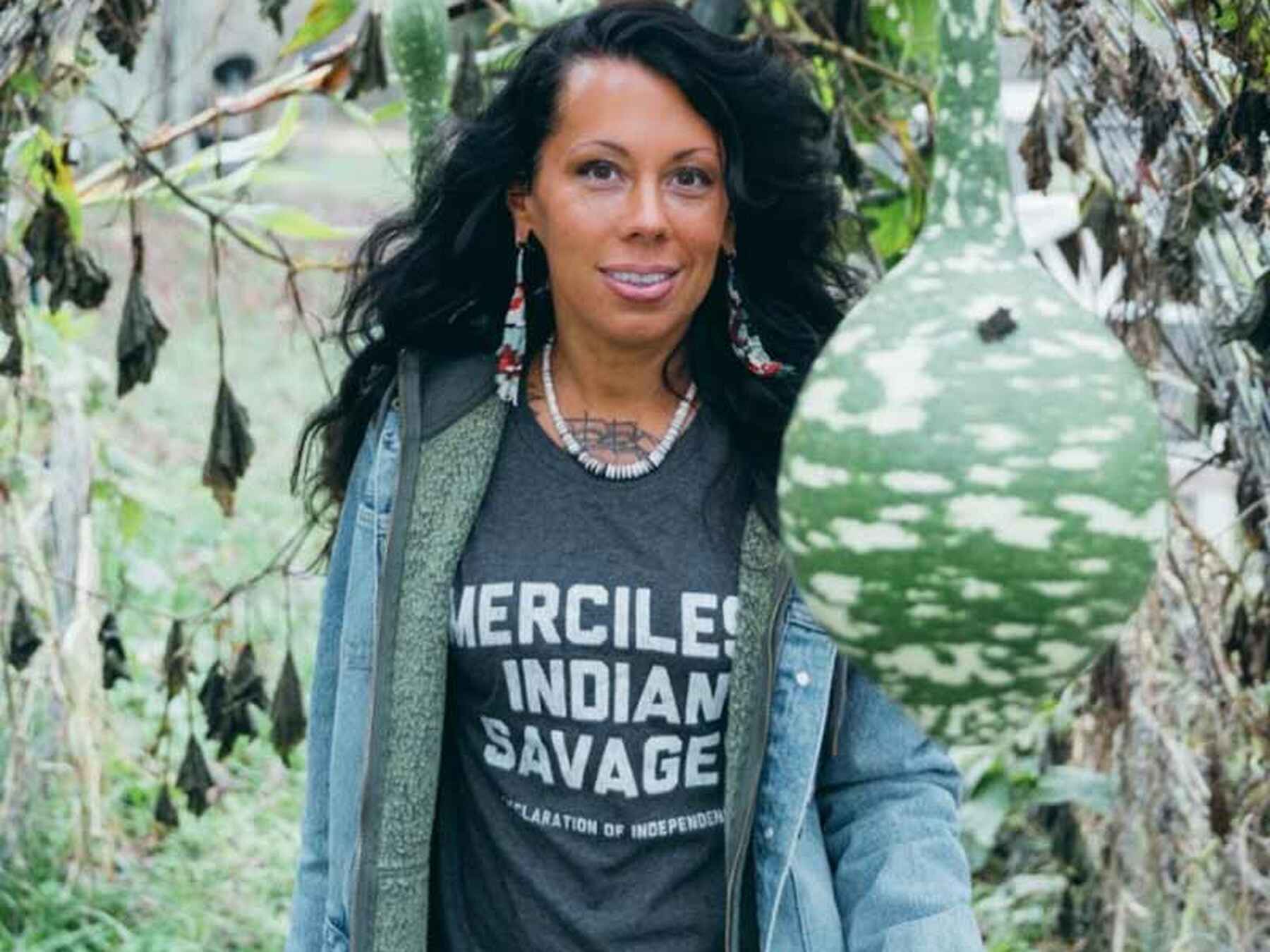 Amyrose Foll stands among birch trees wearing a Merciless Indian Savage graphic t-shirt and denim jacket, displaying her commitment to Indigenous advocacy
