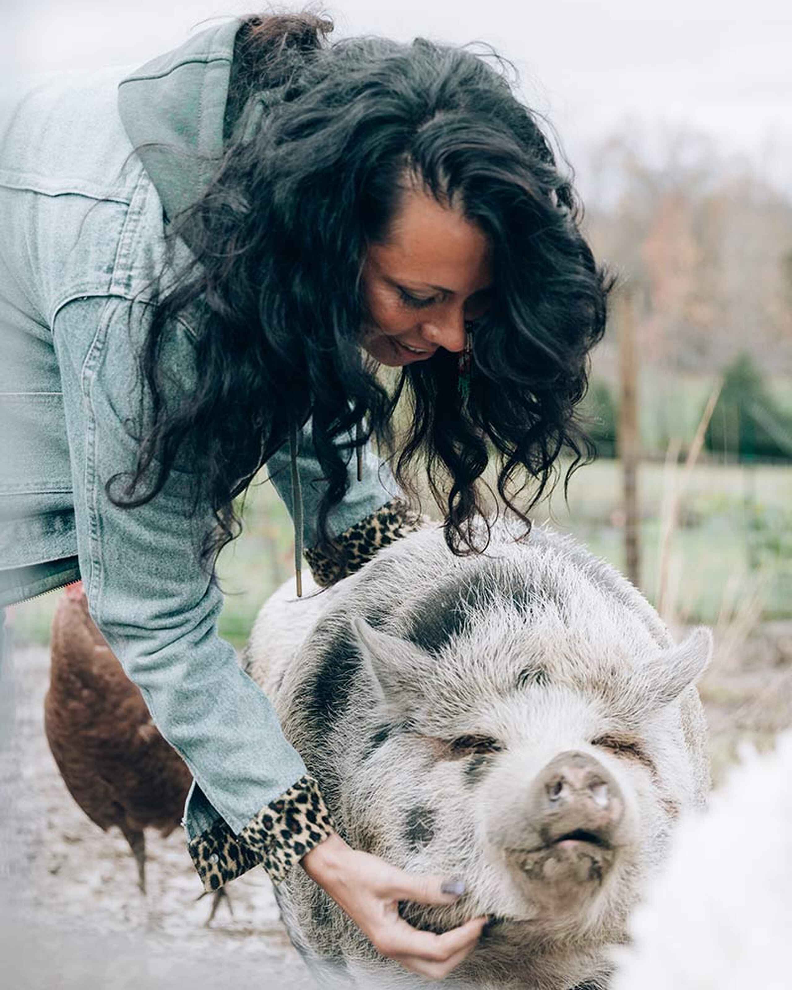 Woman with dark wavy hair petting a white pig on a farm