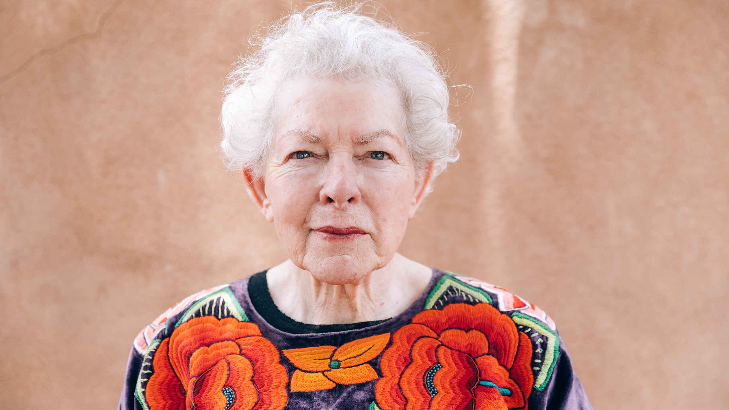 Elderly woman wearing a vibrant embroidered floral shirt with red and orange flowers