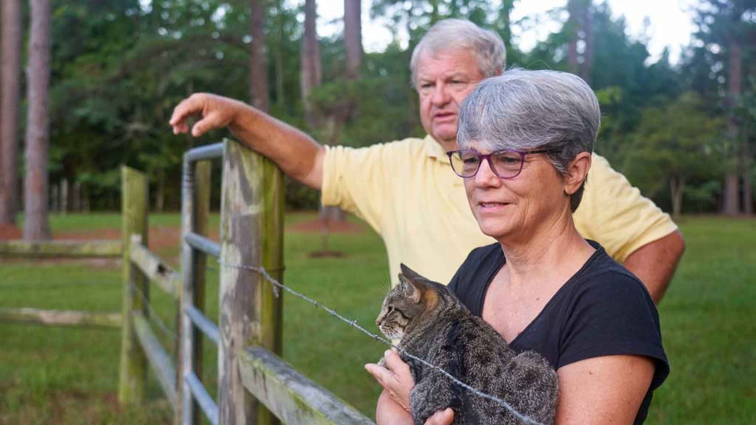 Deb Wray holds a young bobcat while Johnny Wray points toward the pasture on their farm