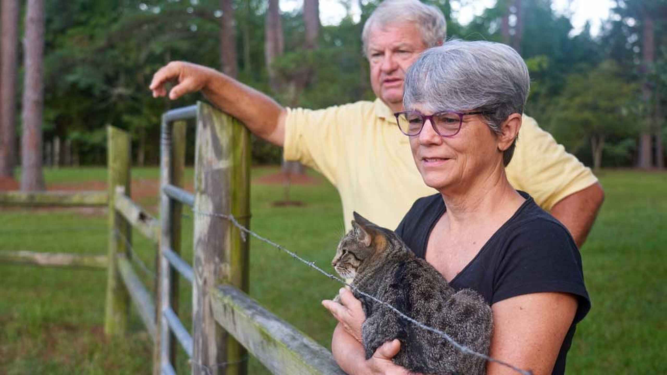 Deb Wray sostiene un lince joven mientras Johnny Wray se&ntilde;ala hacia el pastizal en su granja