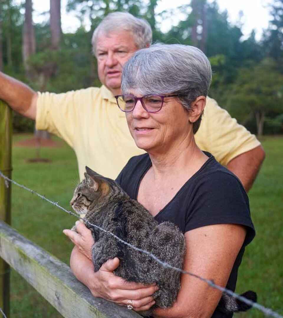 Deb Wray sostiene un lince joven mientras Johnny Wray se&ntilde;ala hacia el pastizal en su granja