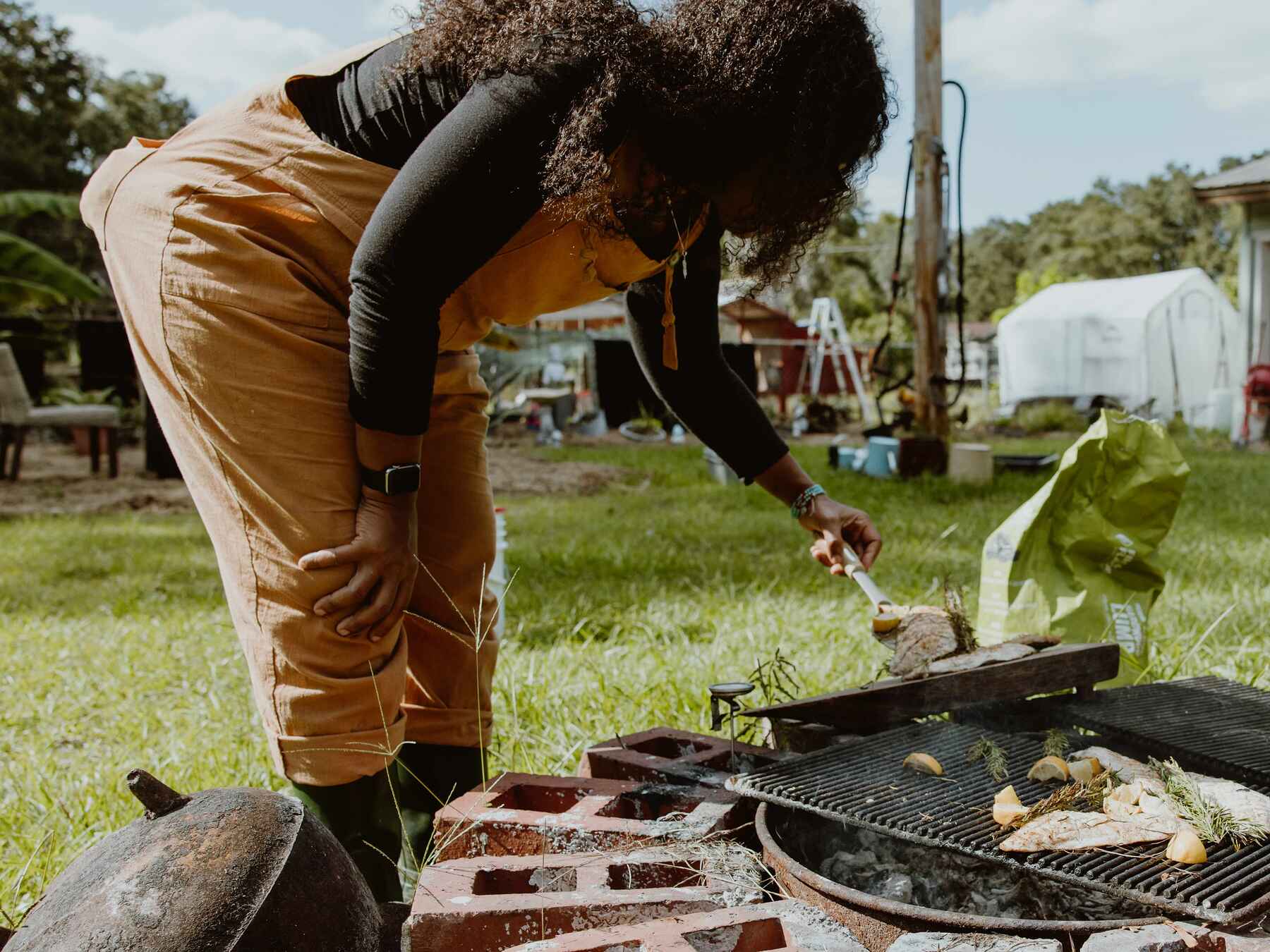 Woman tending a fire pit with grill grates at a community farm gathering