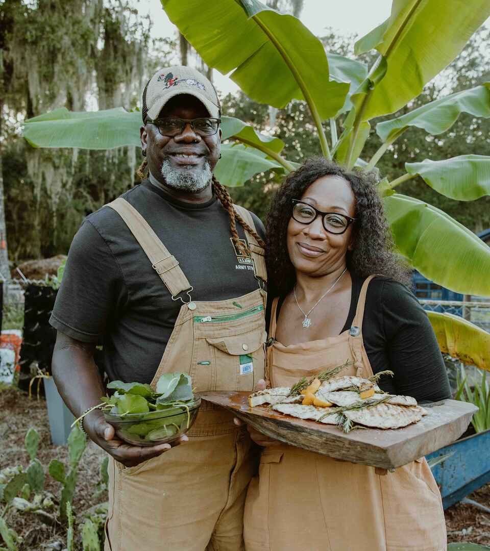 Dos agricultores sosteniendo vegetales frescos y pescado en un huerto con plantas de pl&aacute;tano