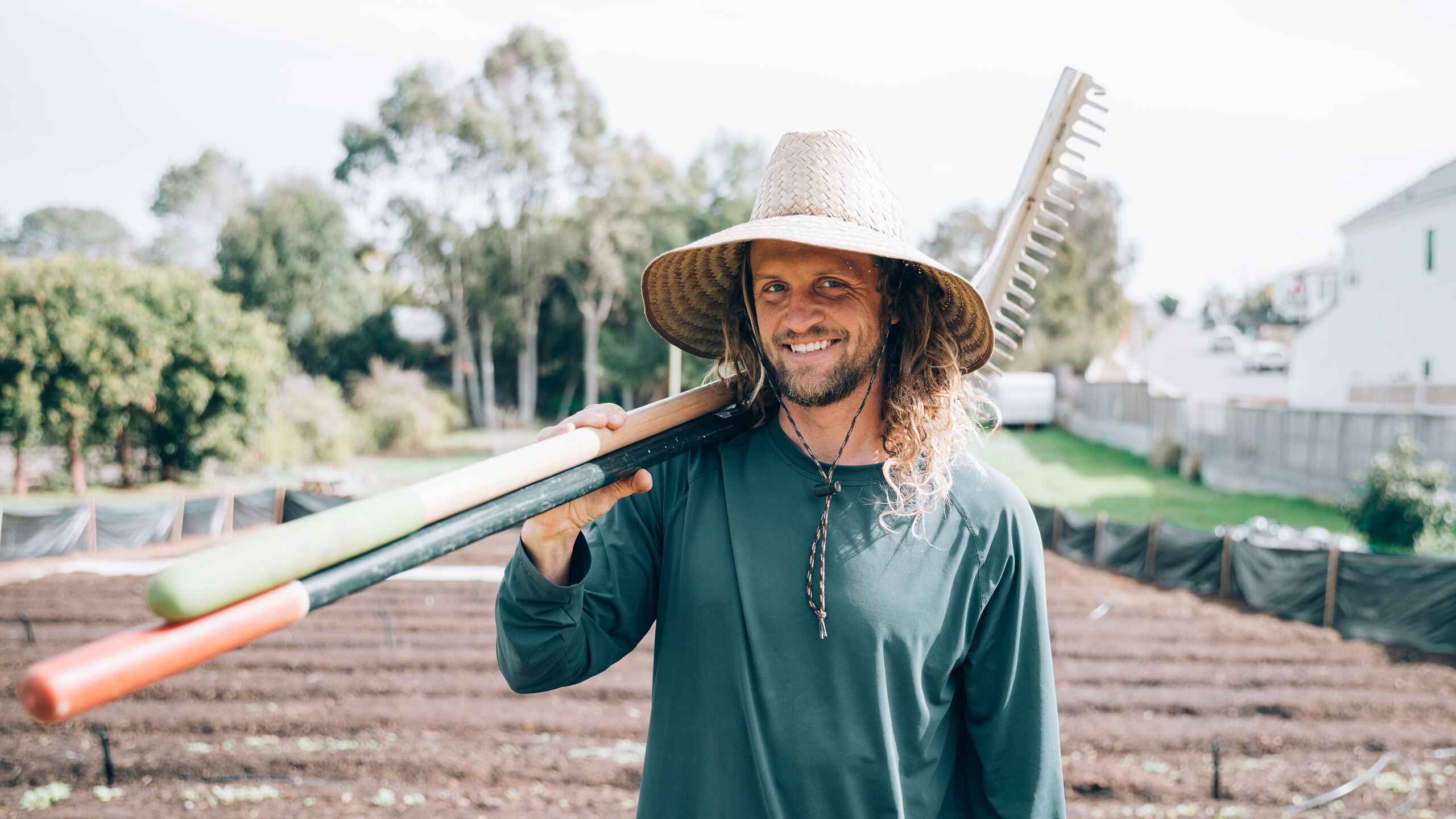 Greg Reese holds a rake over his shoulder while standing in a farm field