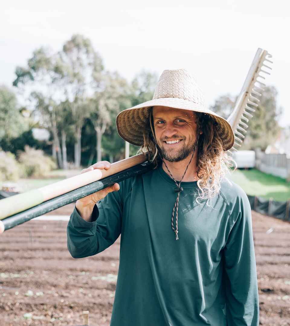 Greg Reese holds a rake over his shoulder while standing in a farm field