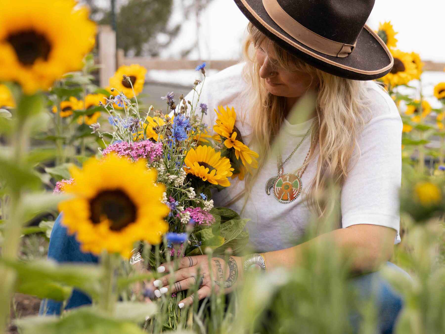 Woman in a cowboy hat holding a bouquet of sunflowers and wildflowers in a sunflower field