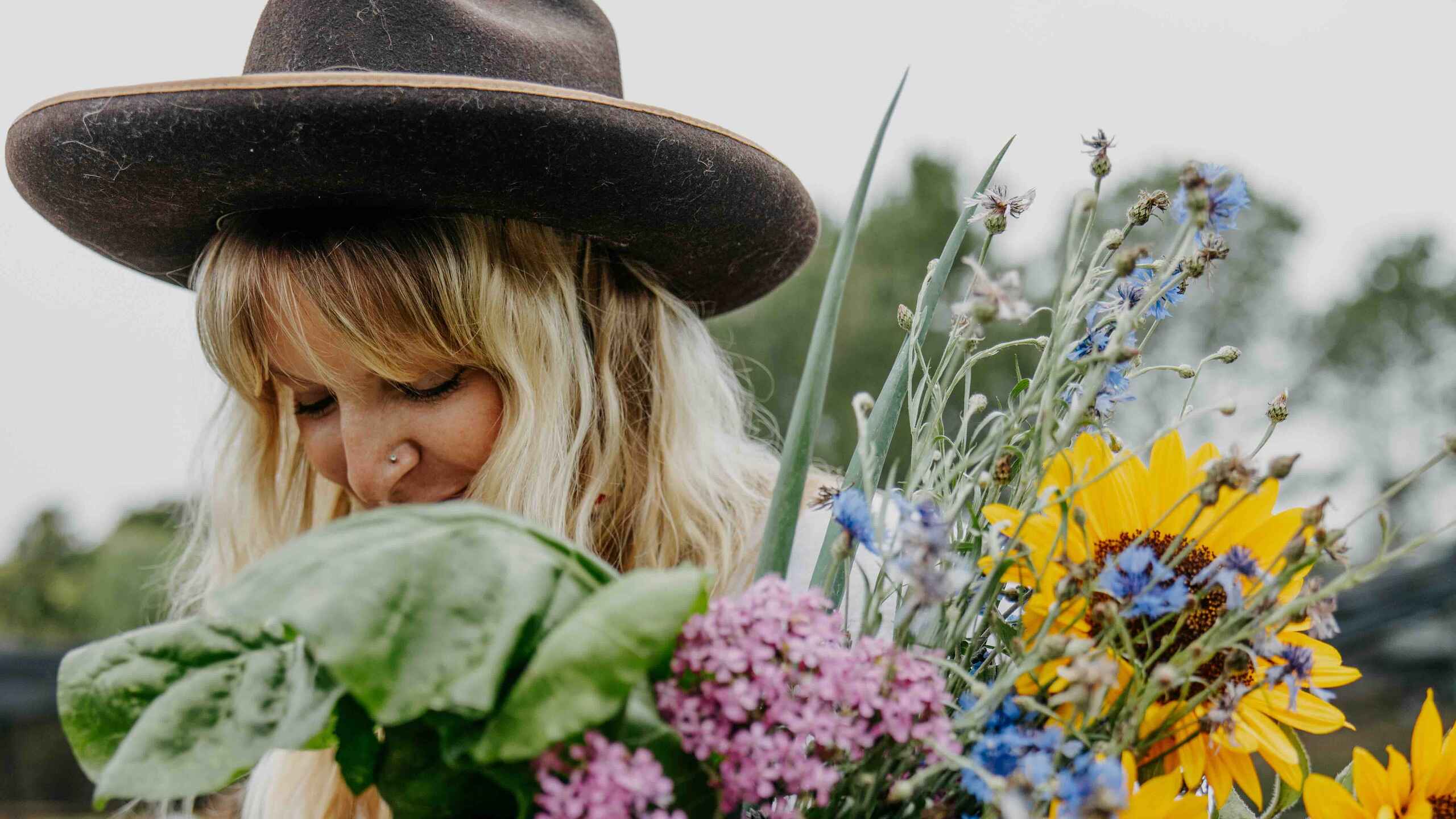 Woman holding a large bouquet of freshly harvested vegetables and flowers from a farm garden