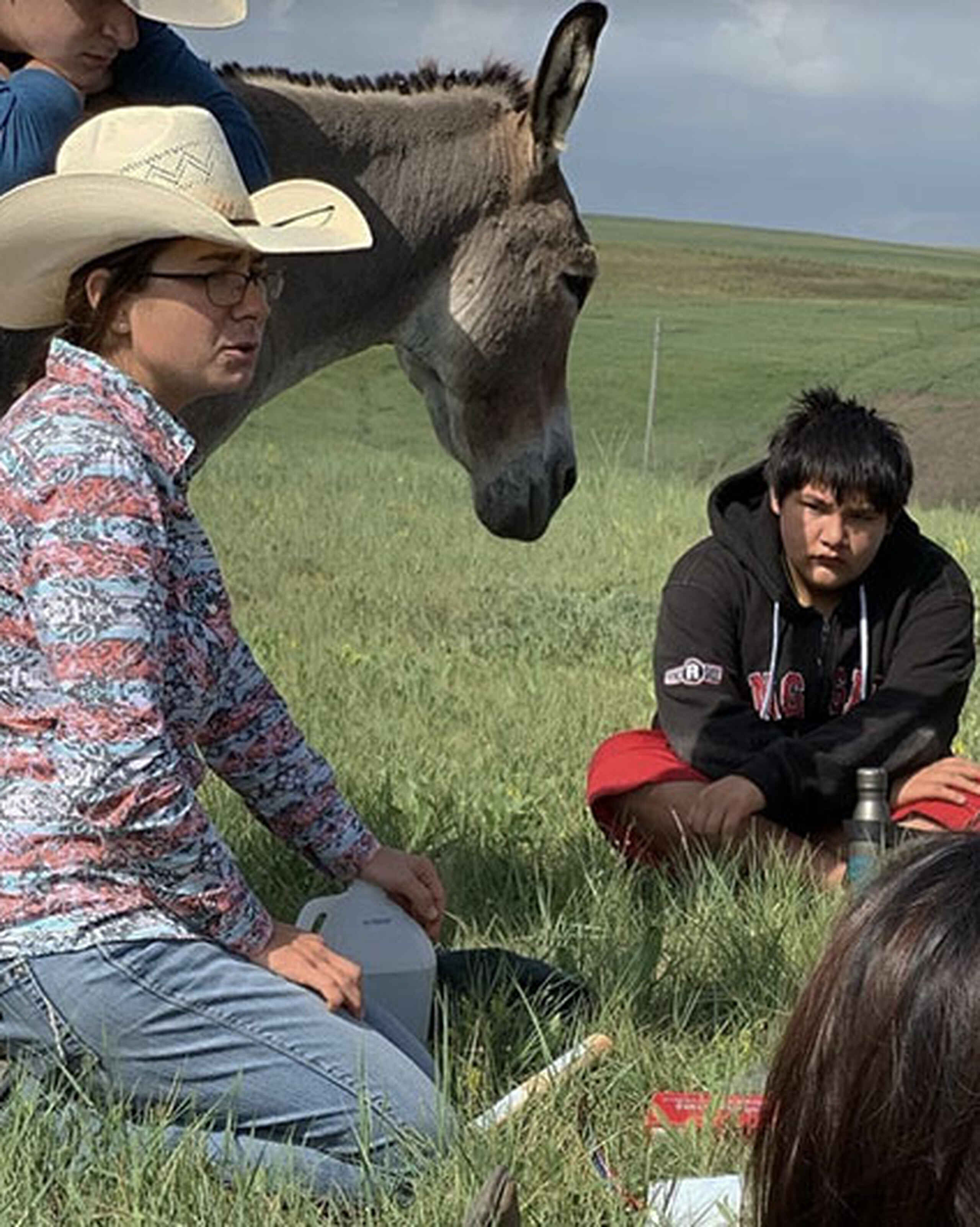 Kelsey Ducheneaux teaches a group of young students about sustainable farming practices during a hands-on lesson in a pasture with a donkey