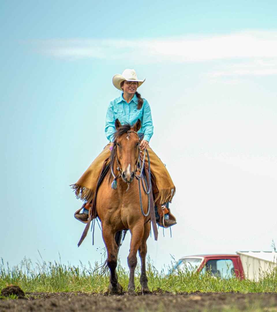 Cowgirl on horseback overlooking a ranch with a red truck and barn in the distance