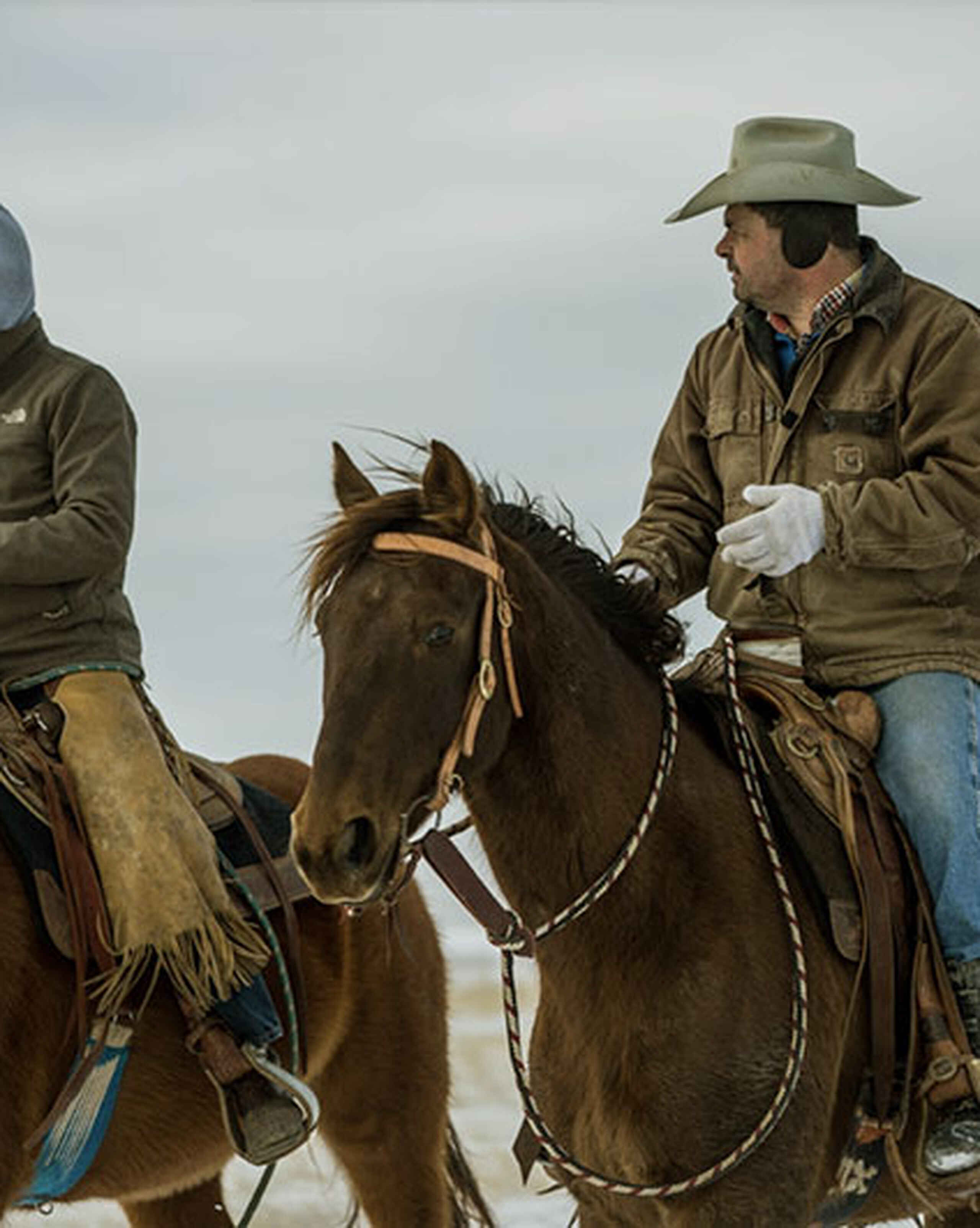 Kelsey Ducheneaux riding horseback across rangeland with a colleague during farm work