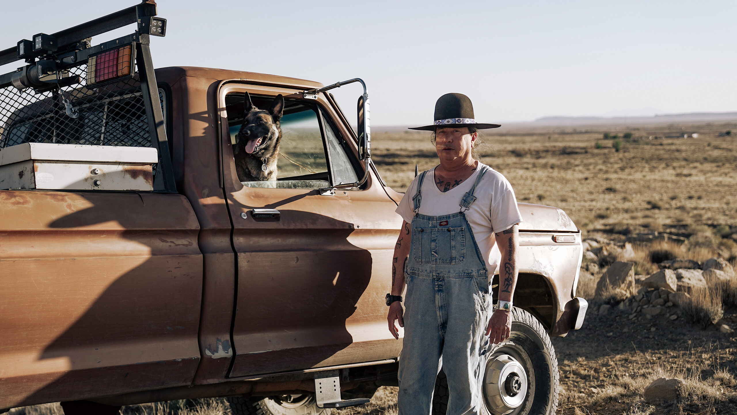 Dr. Michael Kotutwa Johnson stands with his dog beside a work truck on Hopi farmland