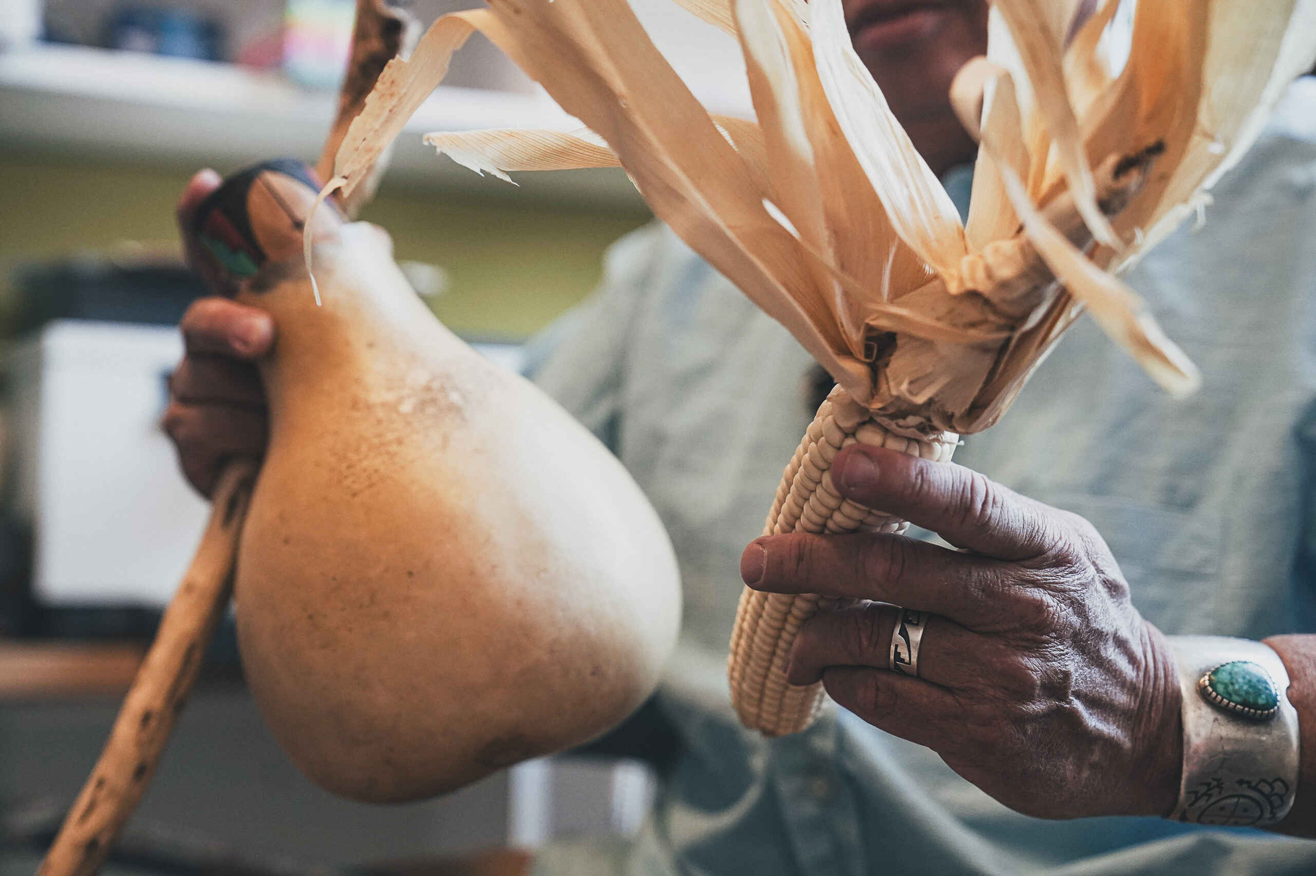 Farmer's hands holding a traditional planting stick and dried corn with husks tied together