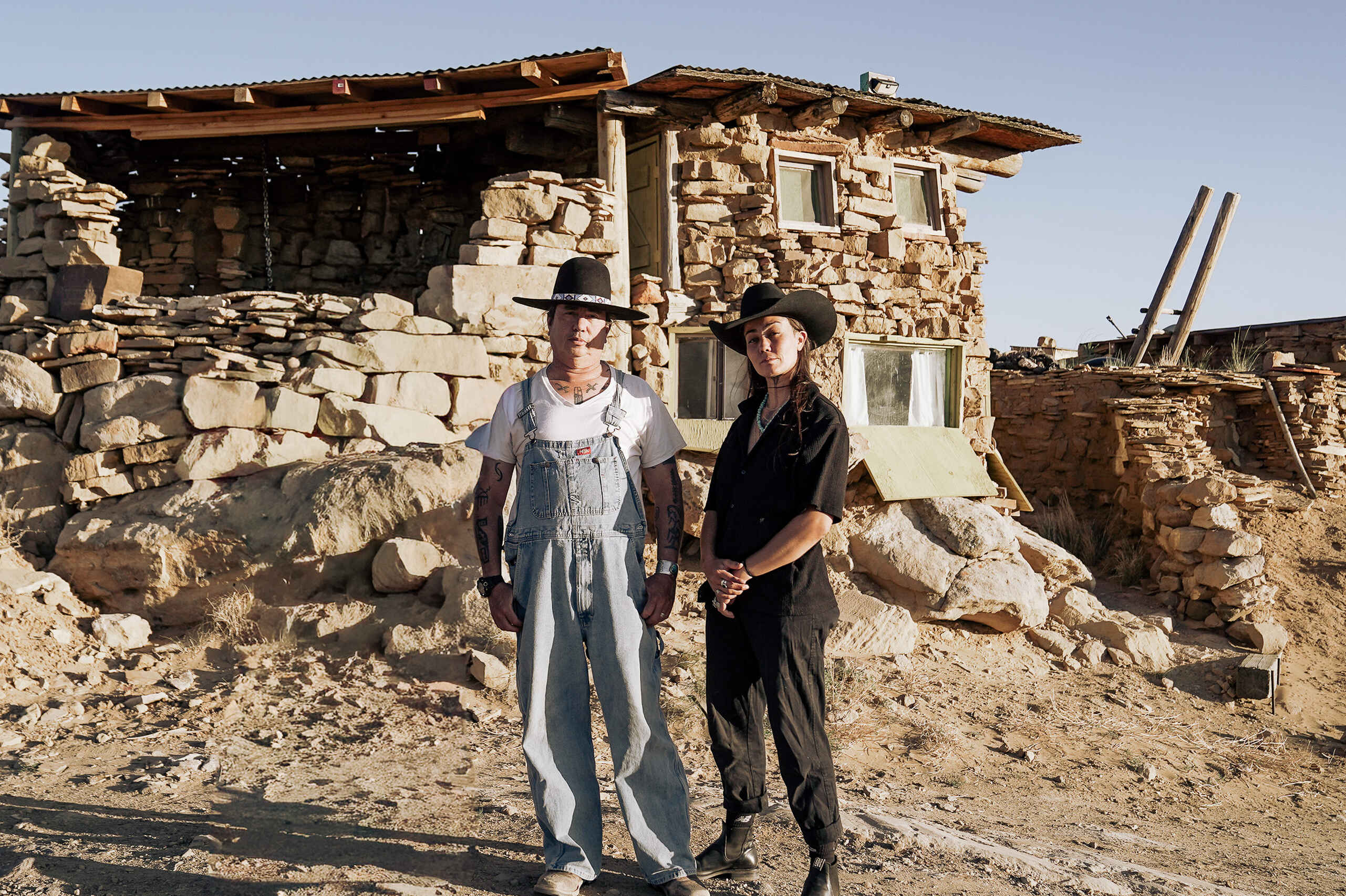 Dr. Michael Kotutwa Johnson and another person stand outside a traditional stone homestead in an arid landscape