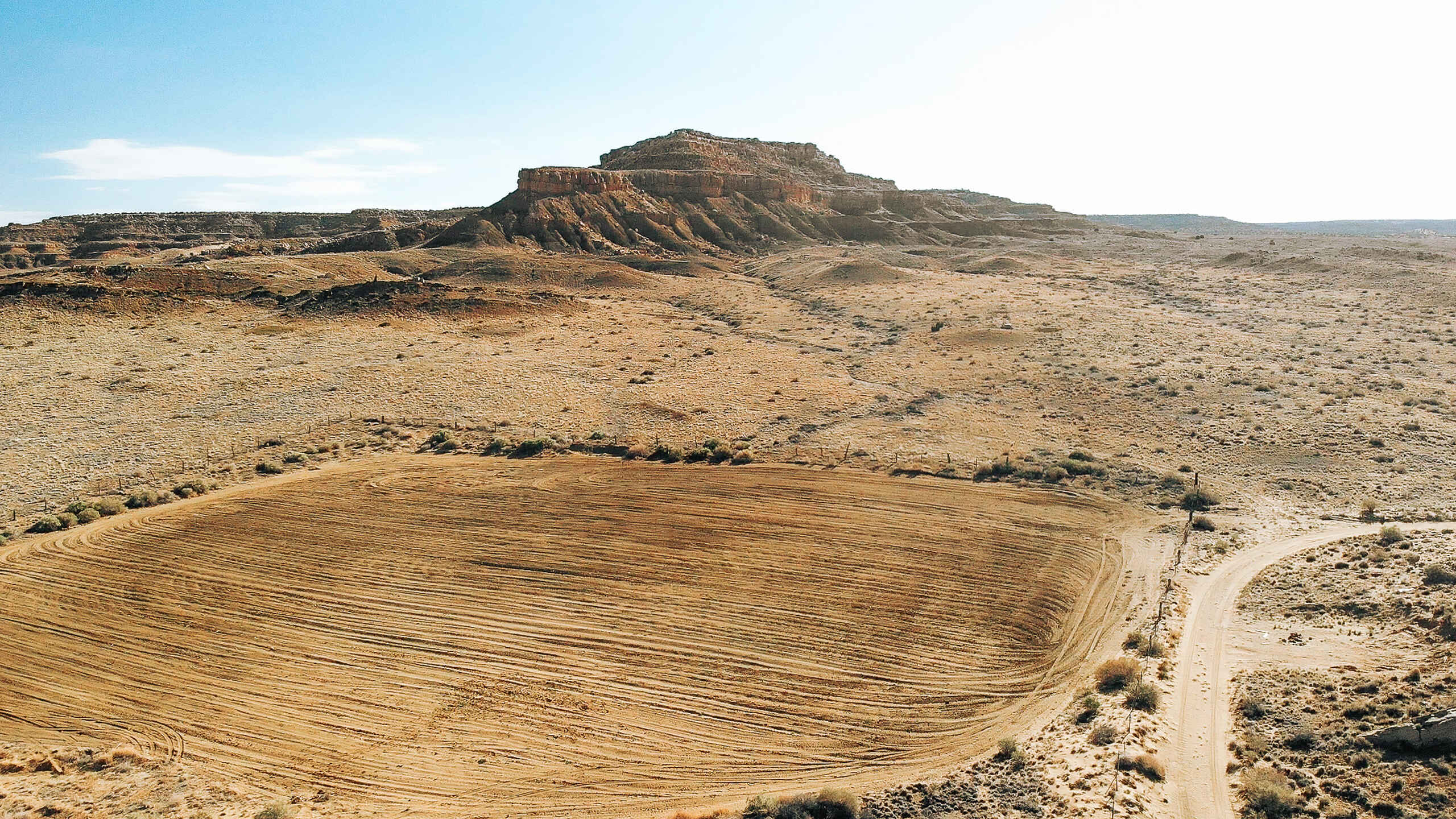 Arid landscape with plowed agricultural field in foreground and mesa formation in background