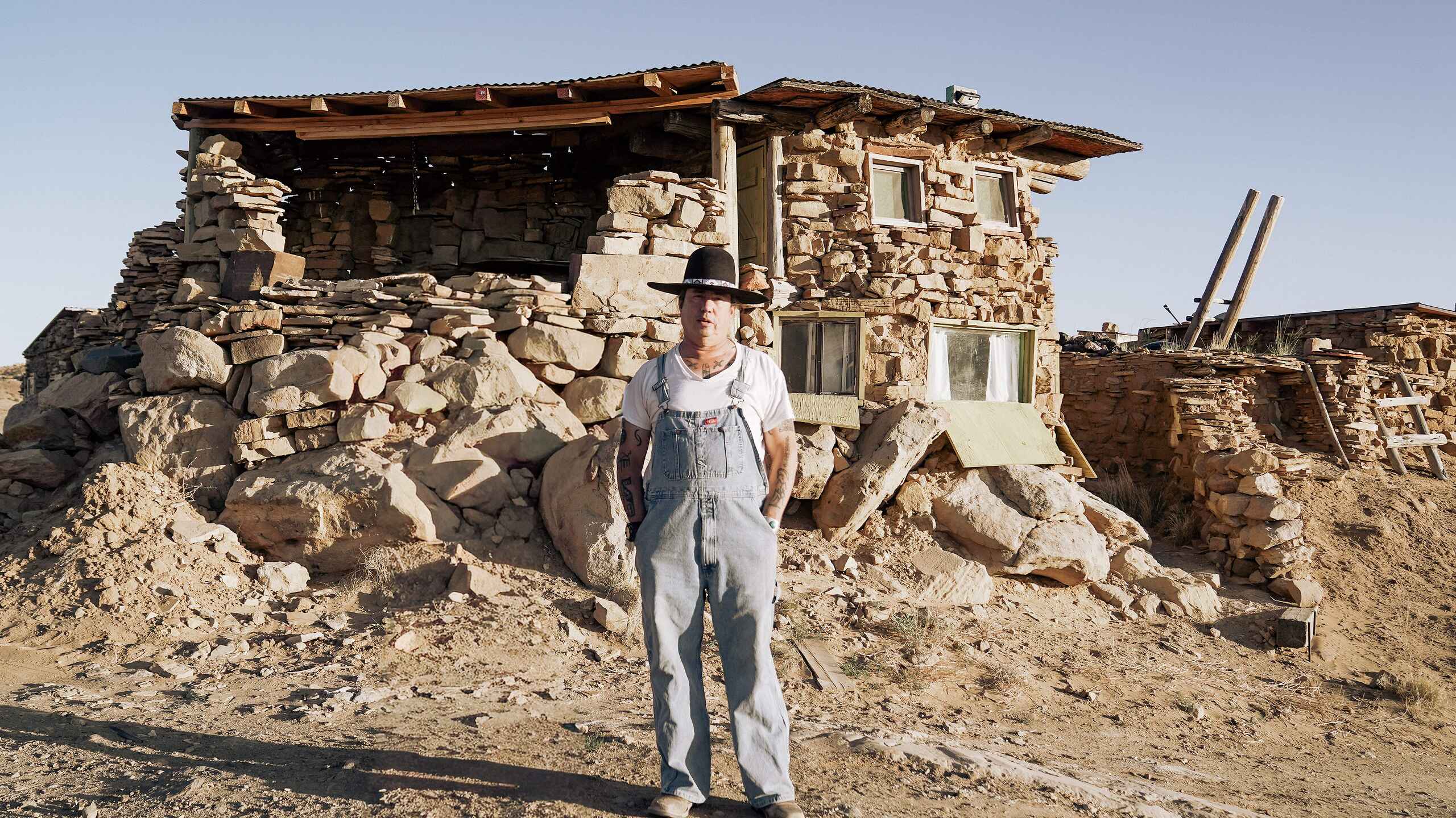 Dr. Michael Kotutwa Johnson stands in front of his traditional stone Hopi house in the desert