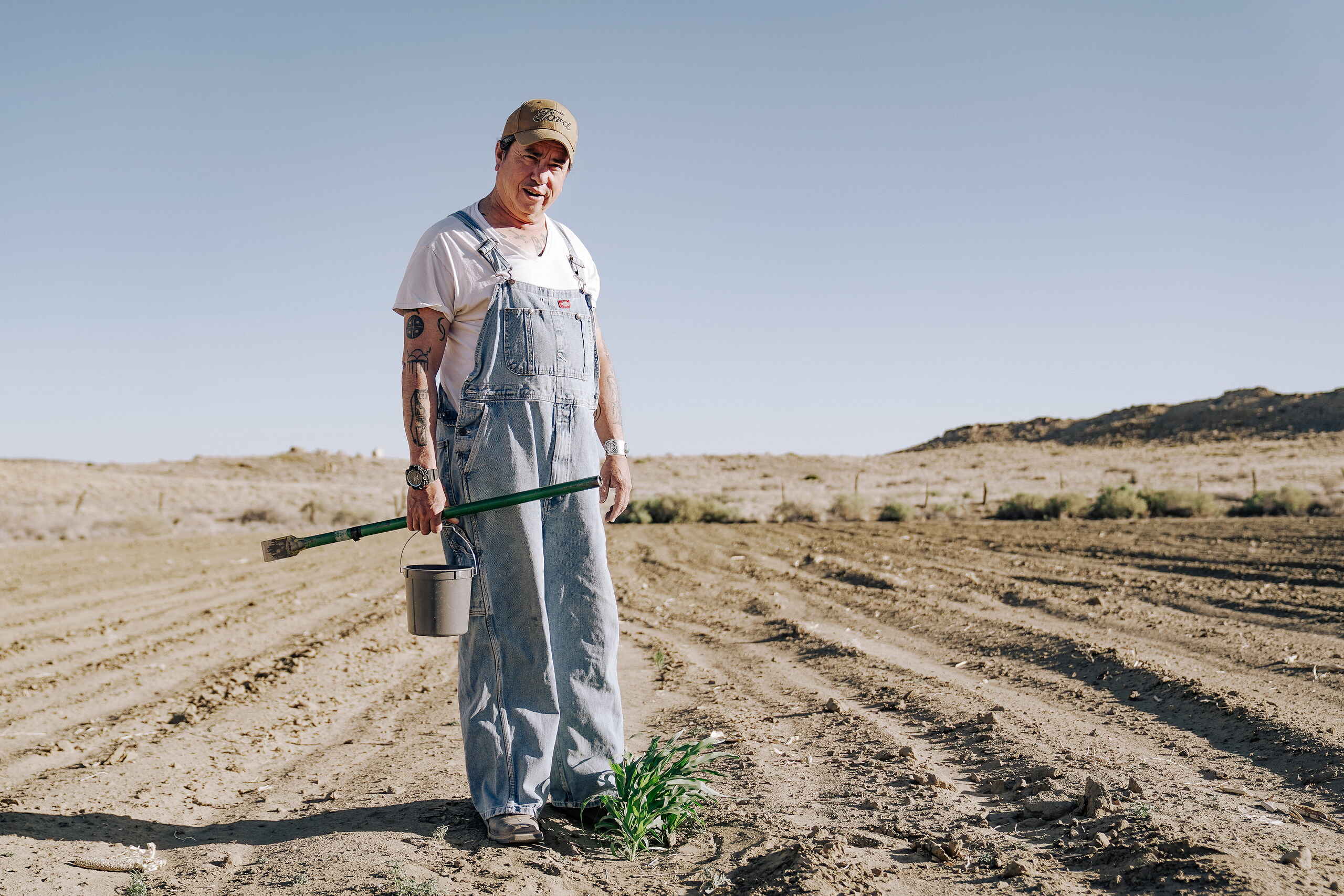 Dr. Michael Kotutwa Johnson stands in a cultivated field holding farming tools