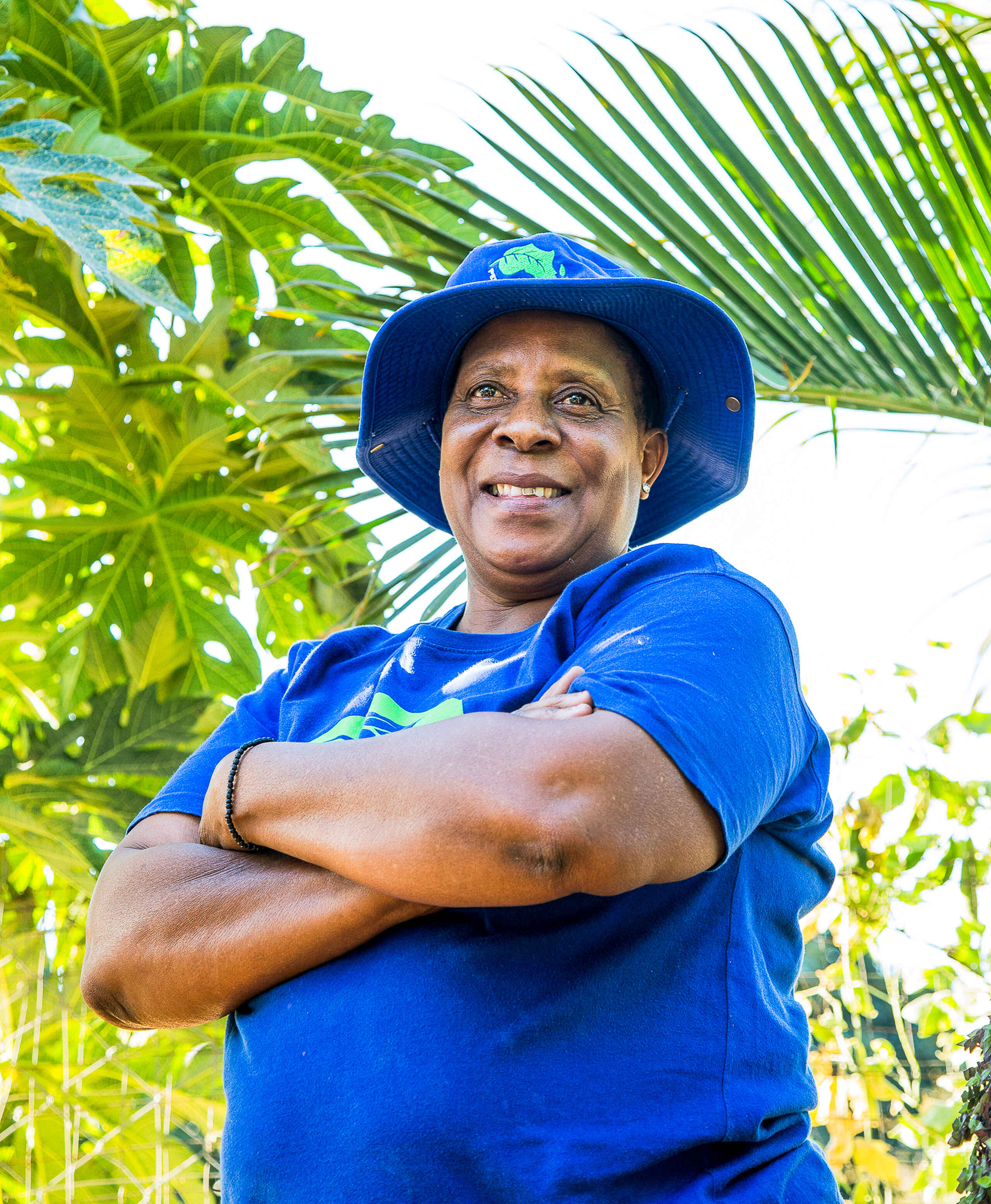 Delinah Nyathi smiles while posing with arms crossed in front of lush green foliage