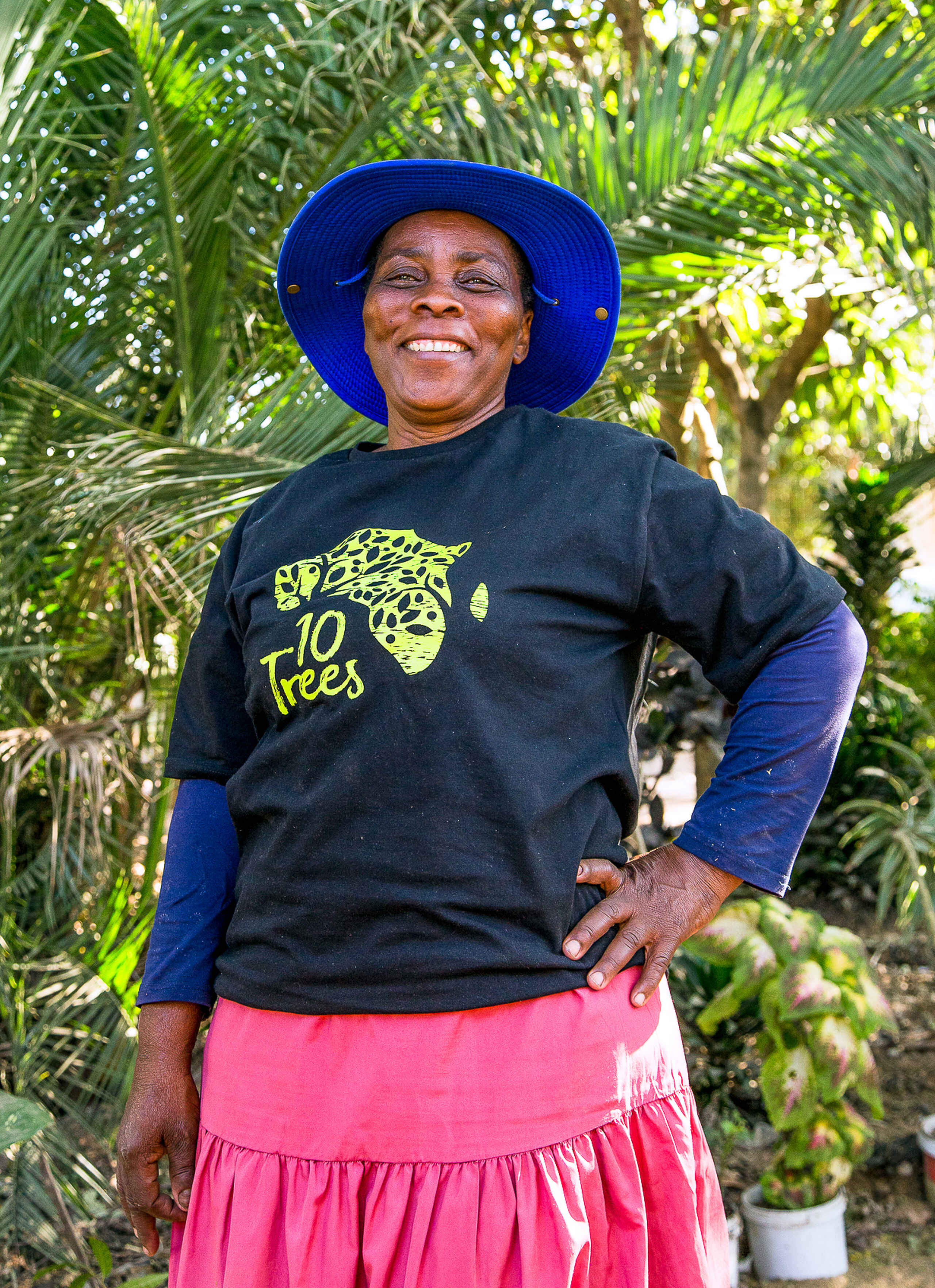 Thandi Manganye smiles while standing in front of palm trees, wearing a blue hat and a 10 Trees t-shirt