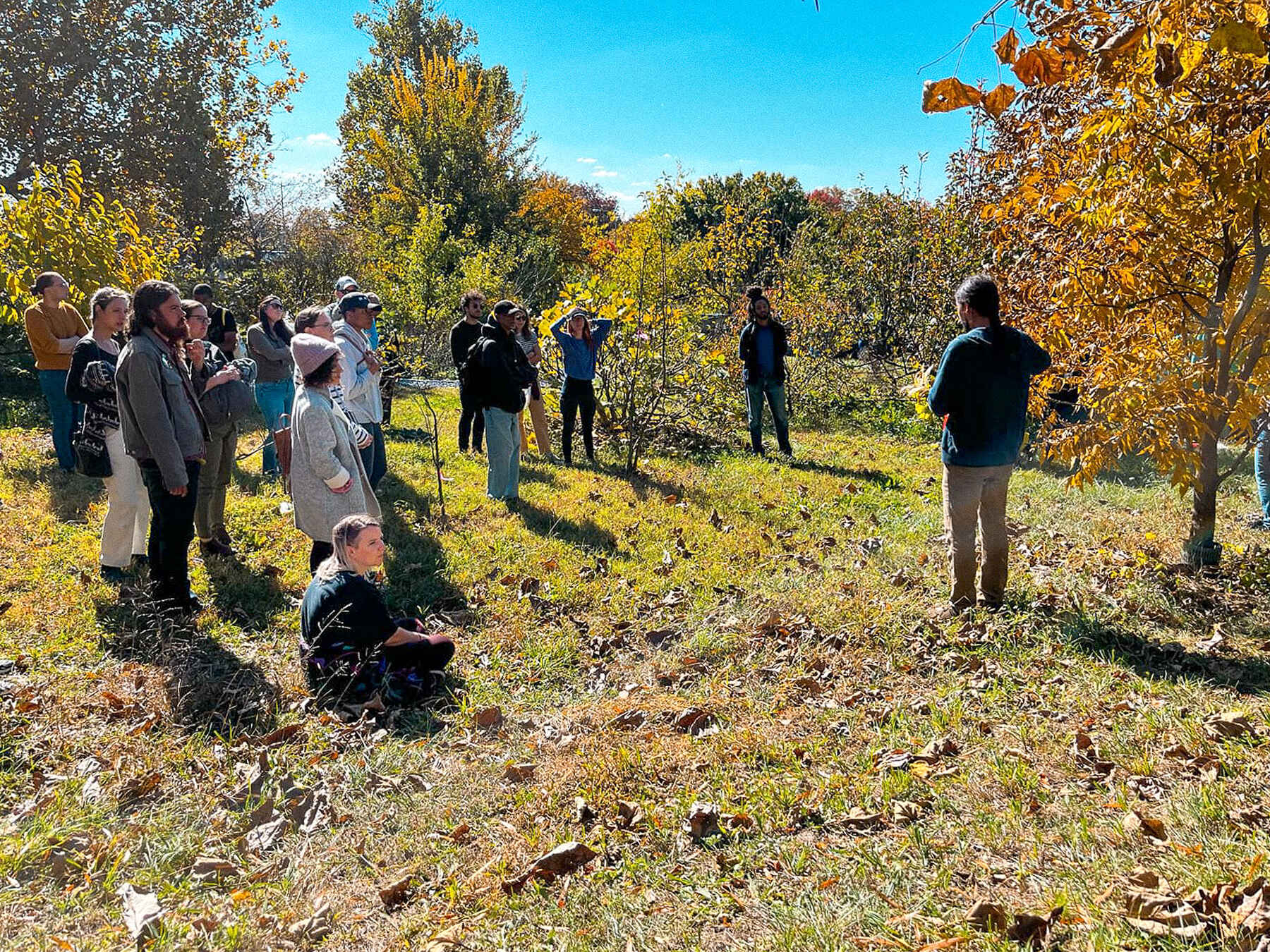 A group of people gathered in an orchard during autumn for an educational farm walk