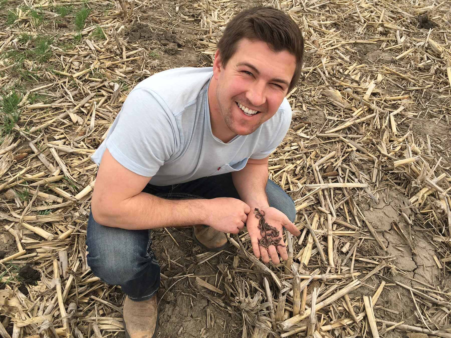 Mitchell Hora smiling while holding healthy soil in his hand at his farm