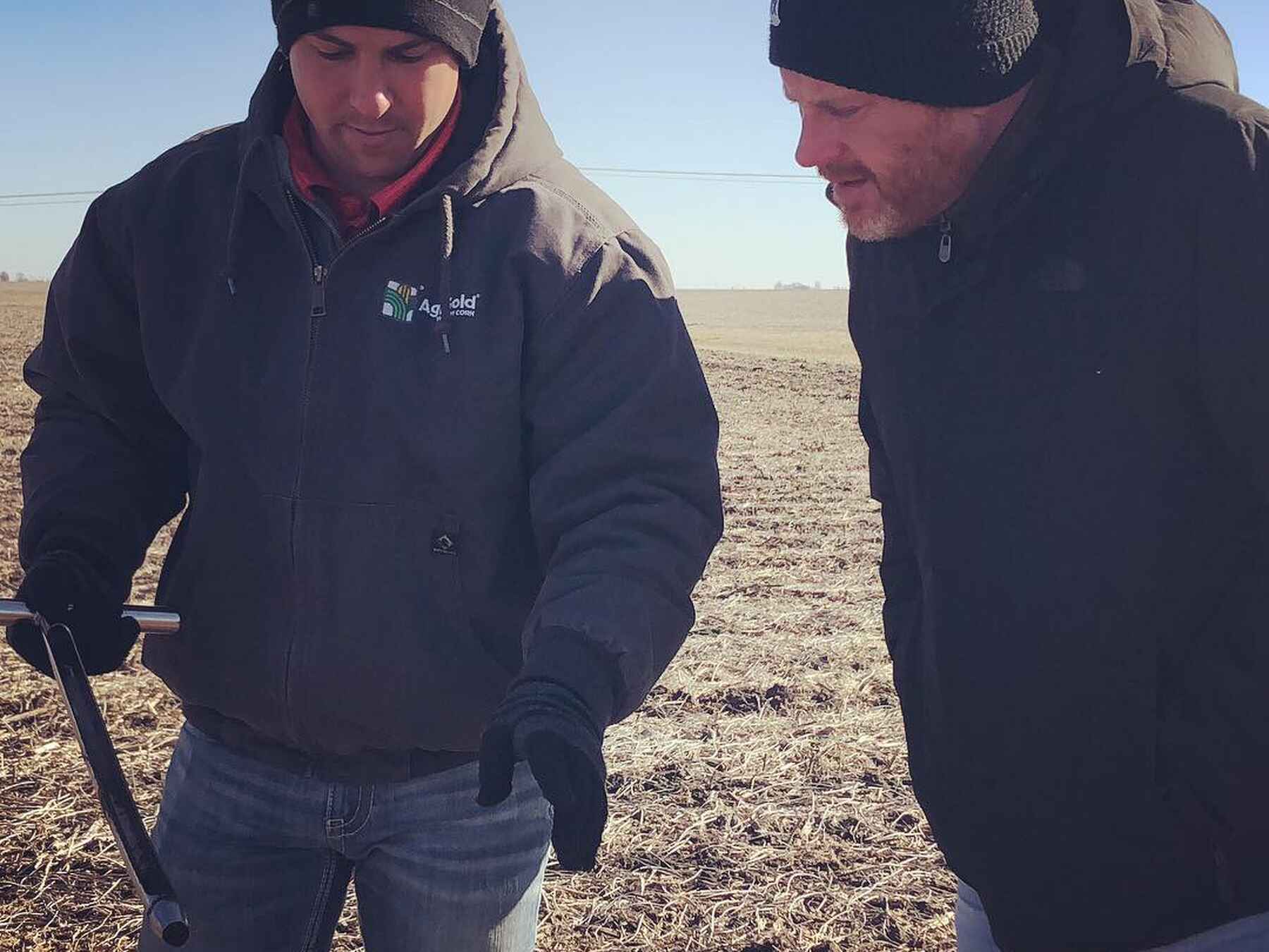 Two men examine soil samples in a harvested field during a farm assessment