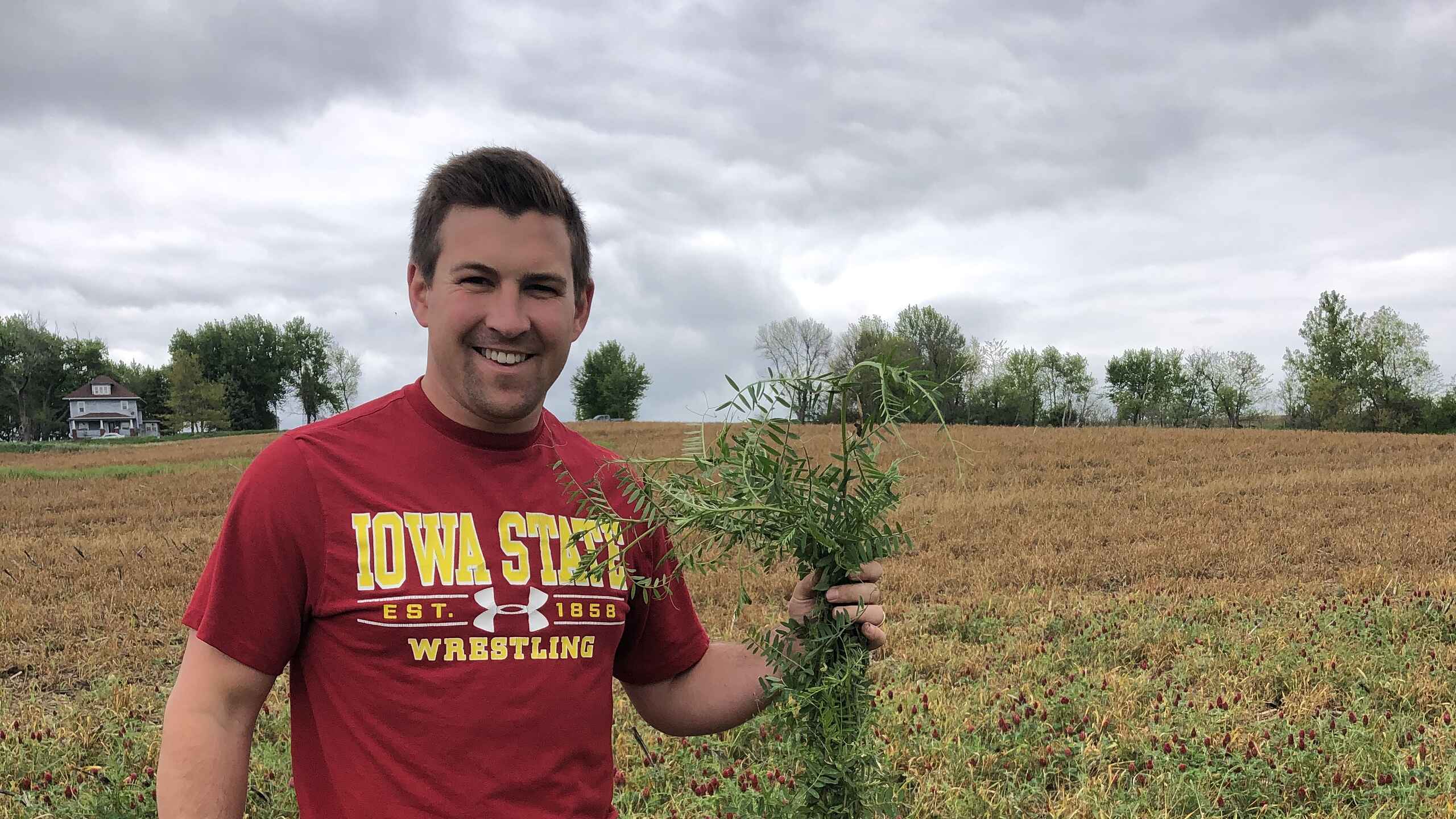 Mitchell Hora holds a soybean plant while standing in his Iowa farm field