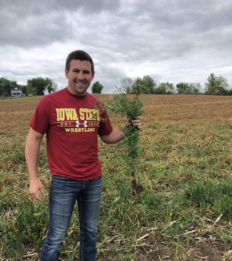 Mitchell Hora sostiene una planta de soya mientras est&aacute; de pie en su campo de granja en Iowa