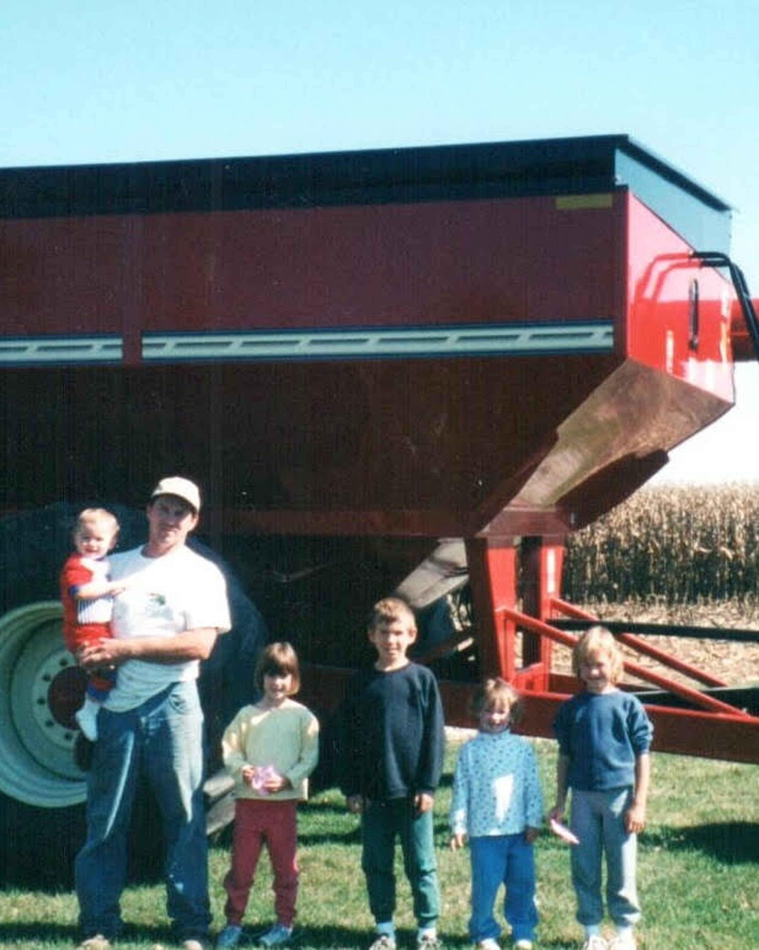 Mitchell Hora and his children stand in front of a Brett grain cart in a cornfield