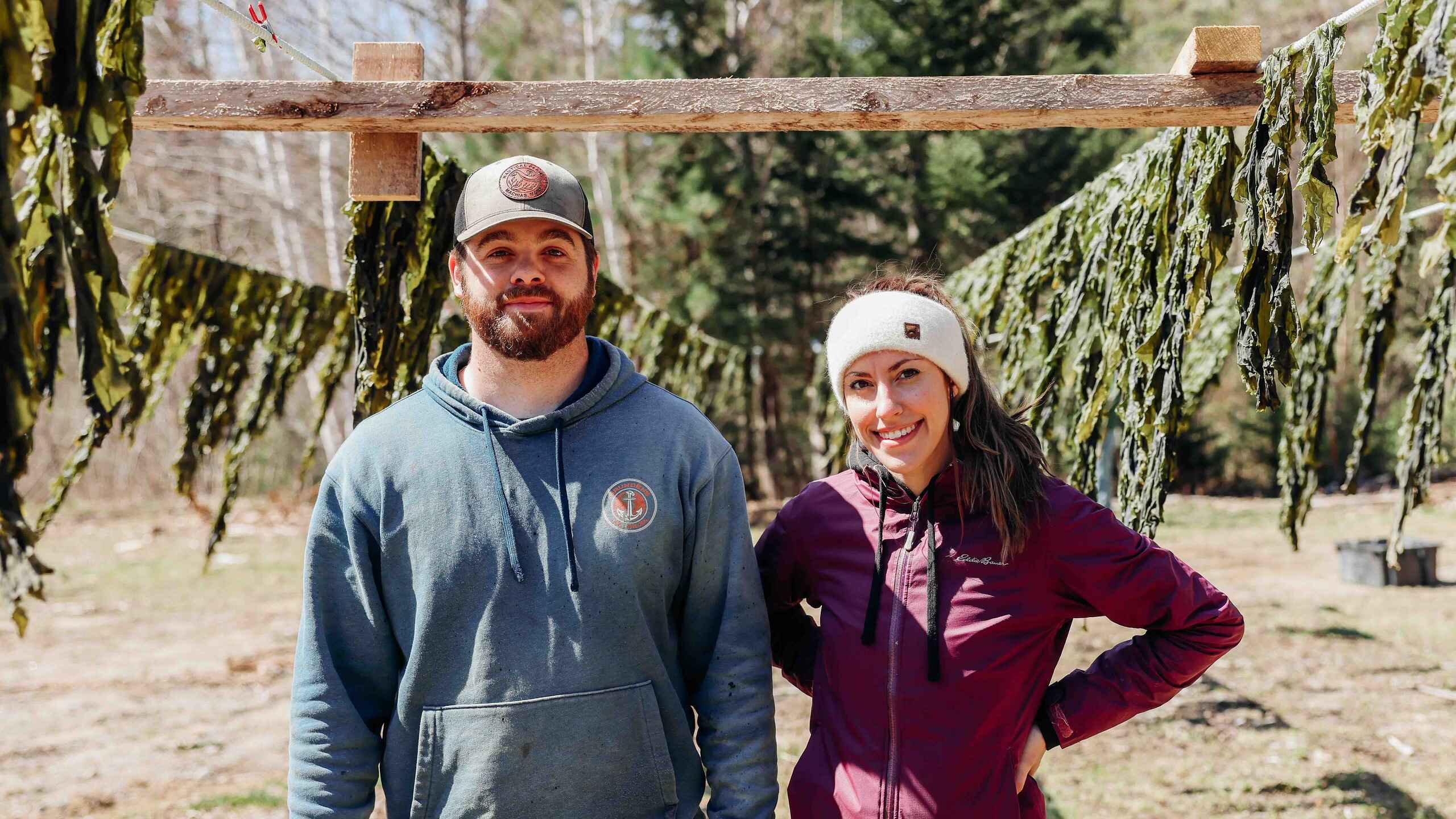 Two farmers stand together under a wooden hop-drying structure at Nautical Farms