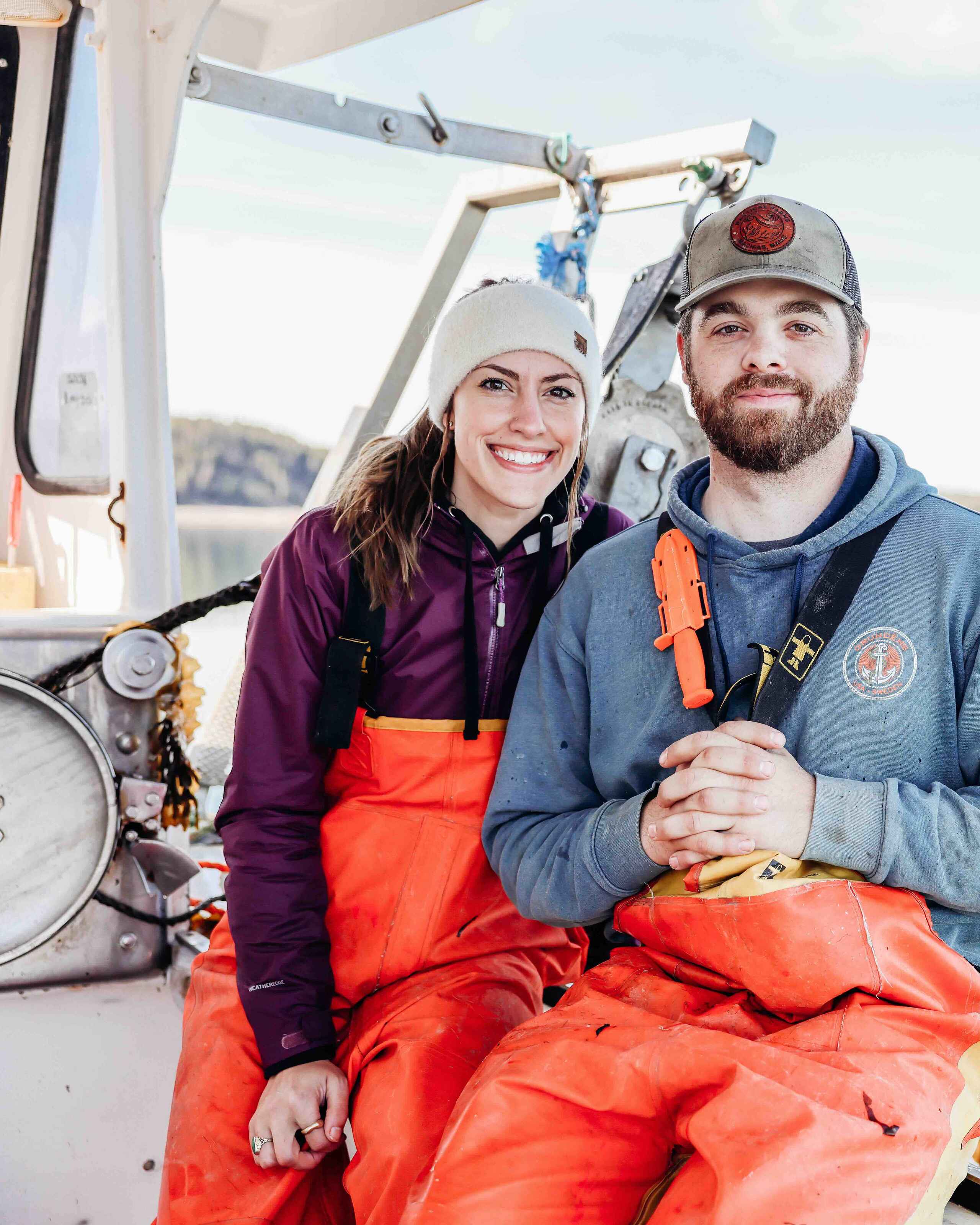 Two people in safety gear sit on a fishing boat holding kelp harvested from the water