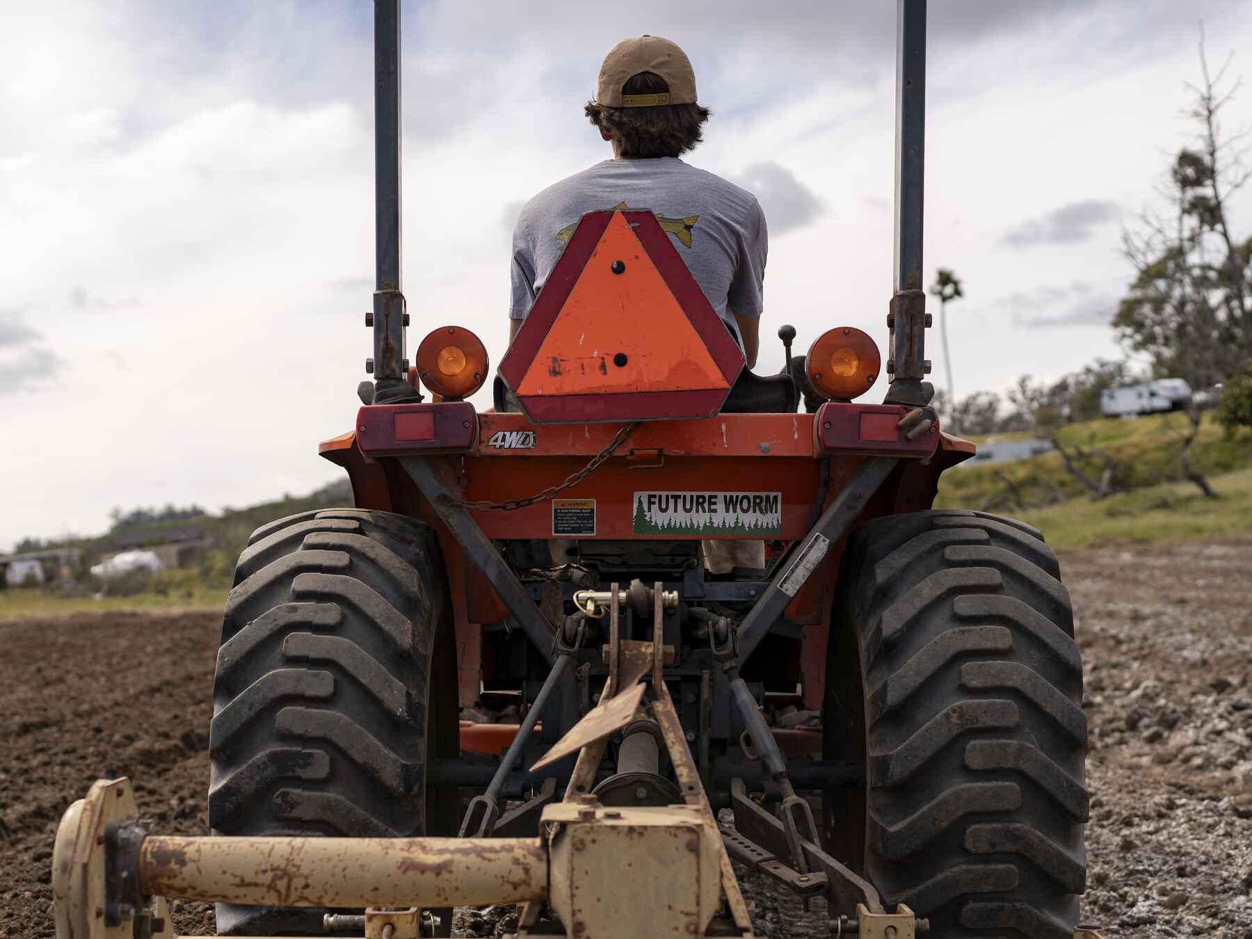 Farmer operating a red Future Worm soil cultivation machine in a plowed field