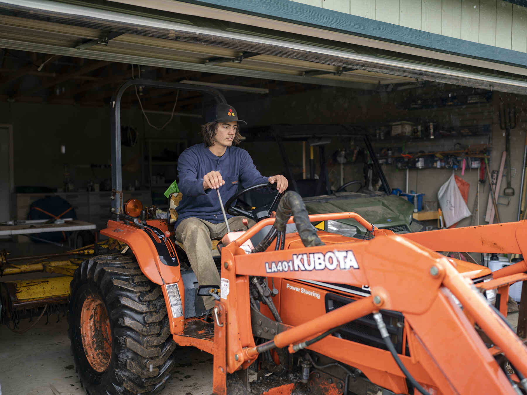 Man operating a Kubota tractor with front-end loader in a farm garage