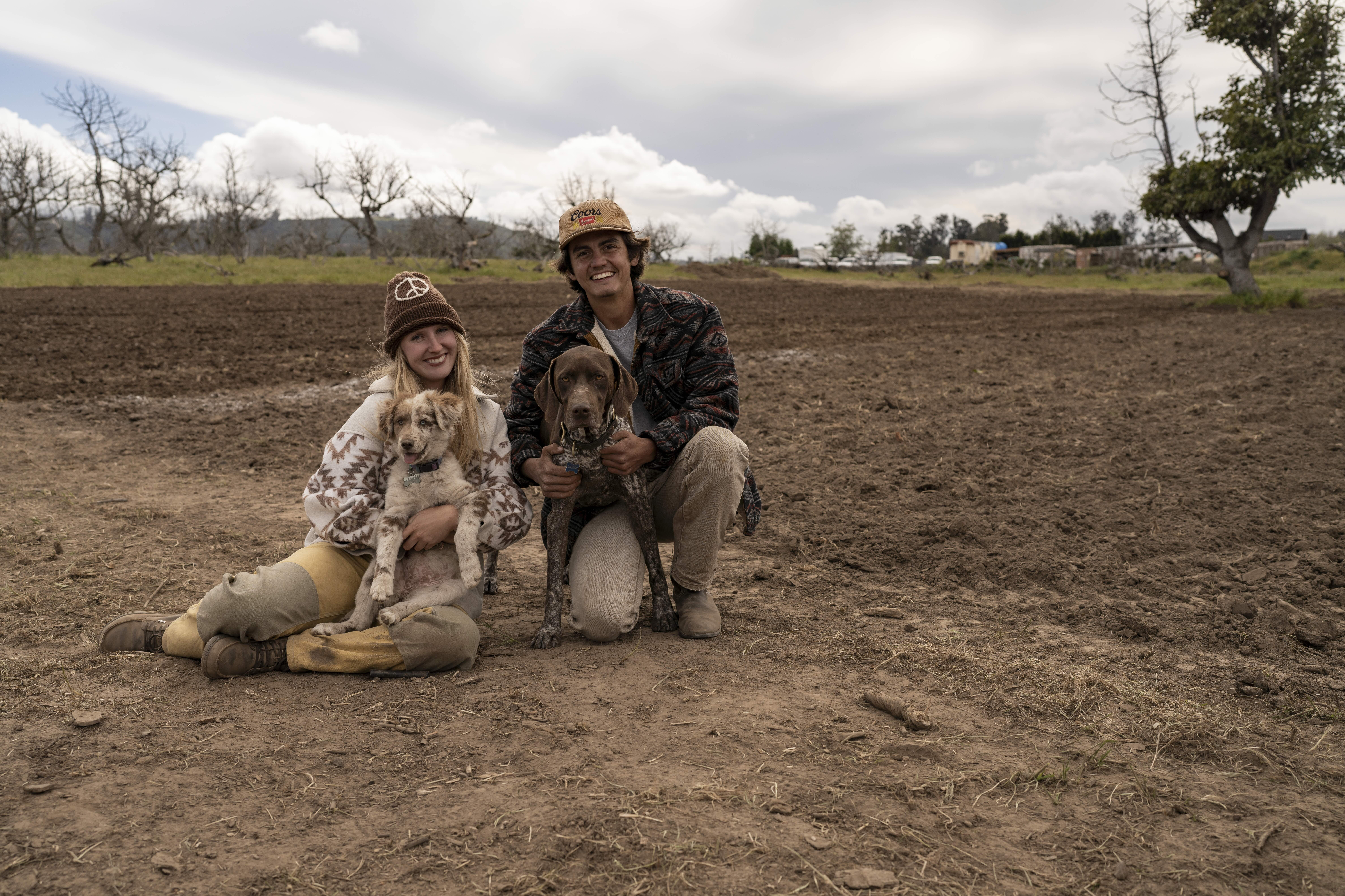 Two farmers kneel with their hunting dogs in a plowed field at Red Tail Farms