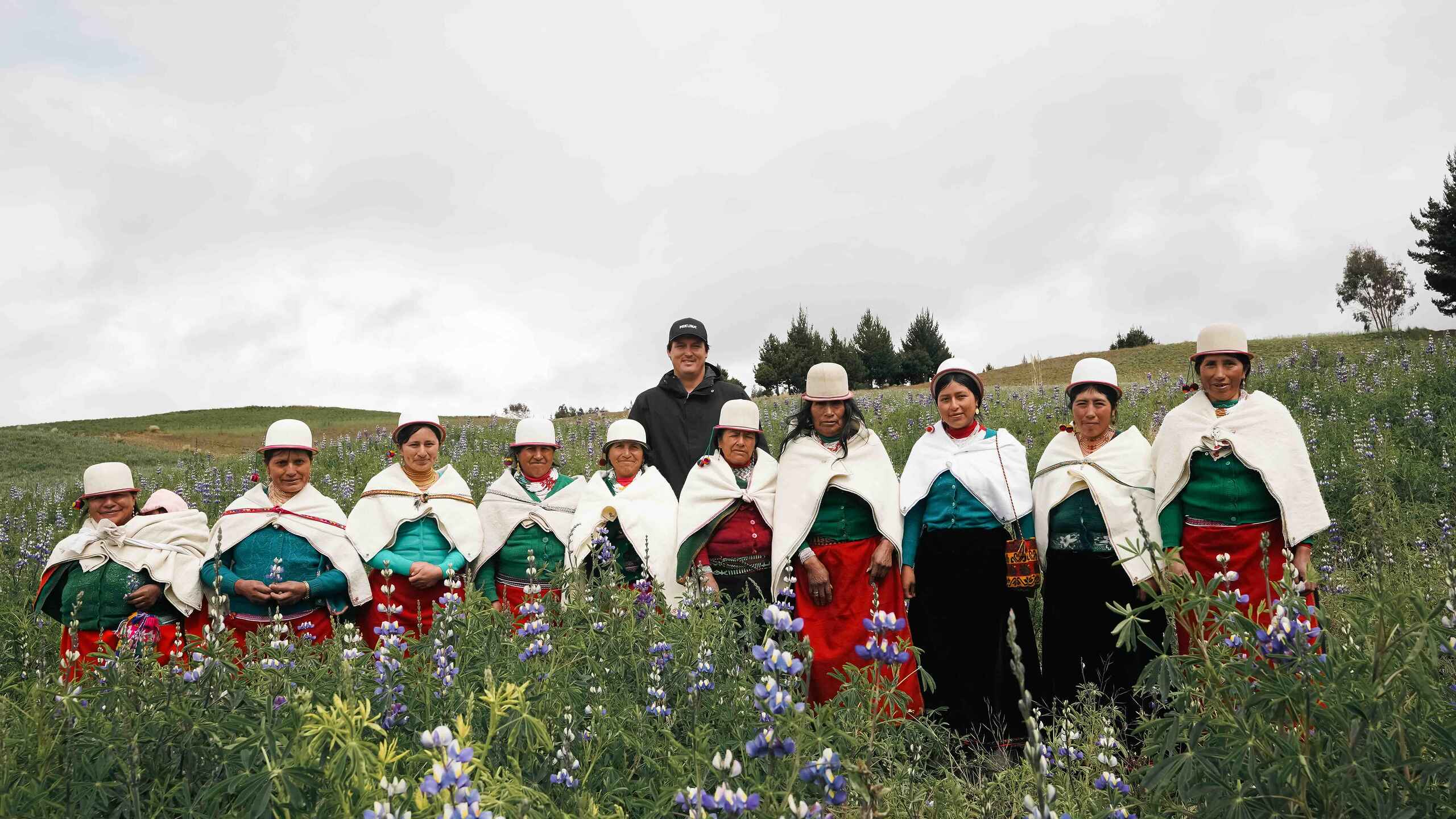 Group of Indigenous Ecuadorian women wearing traditional dress and white hats standing together in a lupine flower field