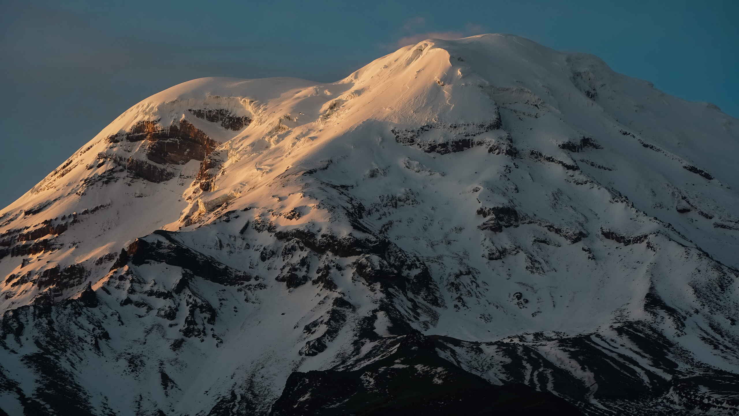 Pico volc&aacute;nico cubierto de nieve iluminado por la luz dorada del sol contra un cielo azul despejado