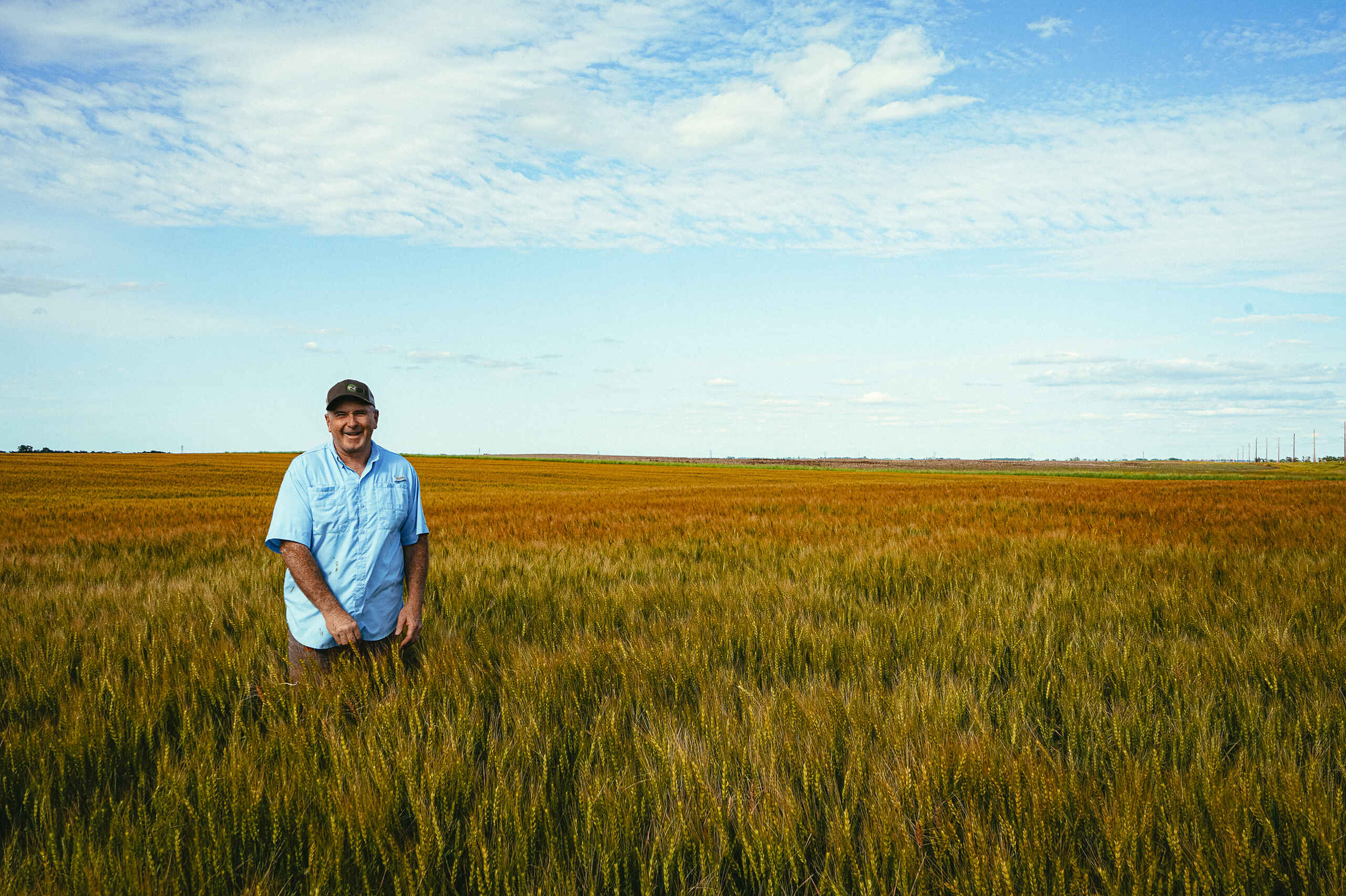 Agricultor de pie en un campo de granos maduro bajo un cielo azul