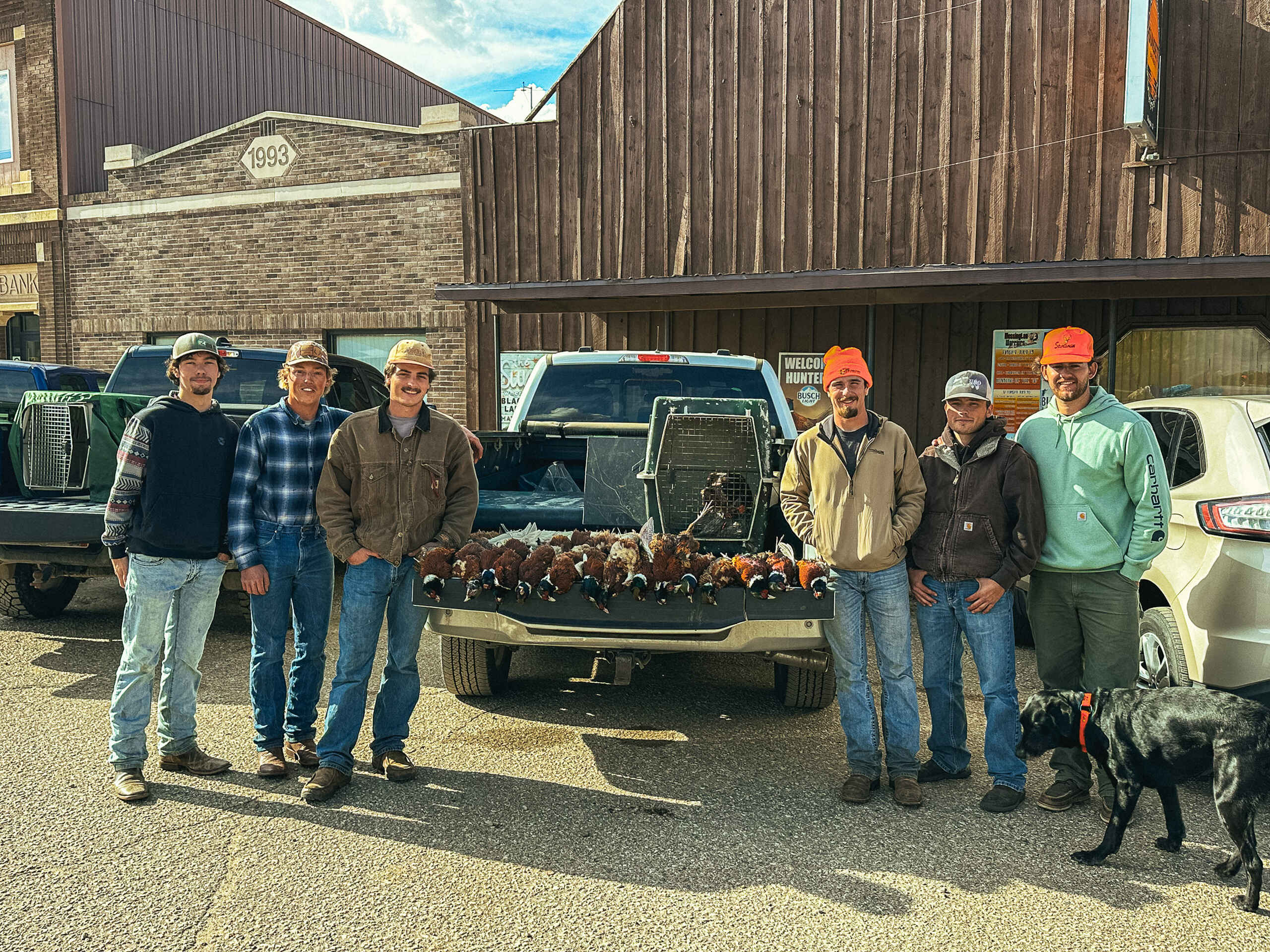 Six farmers and a dog stand with a pickup truck bed full of pheasants after a successful hunt