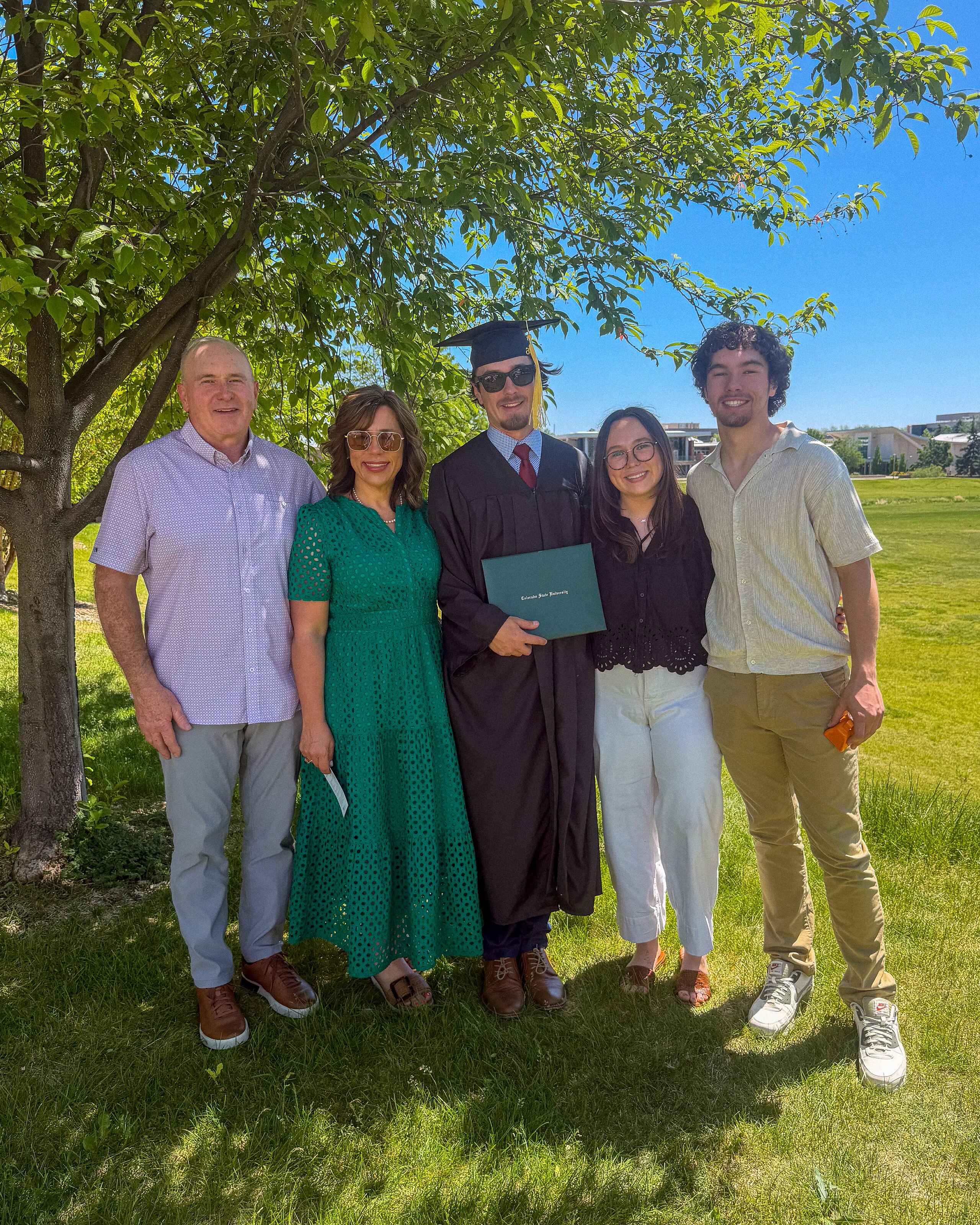 Family celebrating with a graduate holding a diploma at a outdoor commencement ceremony