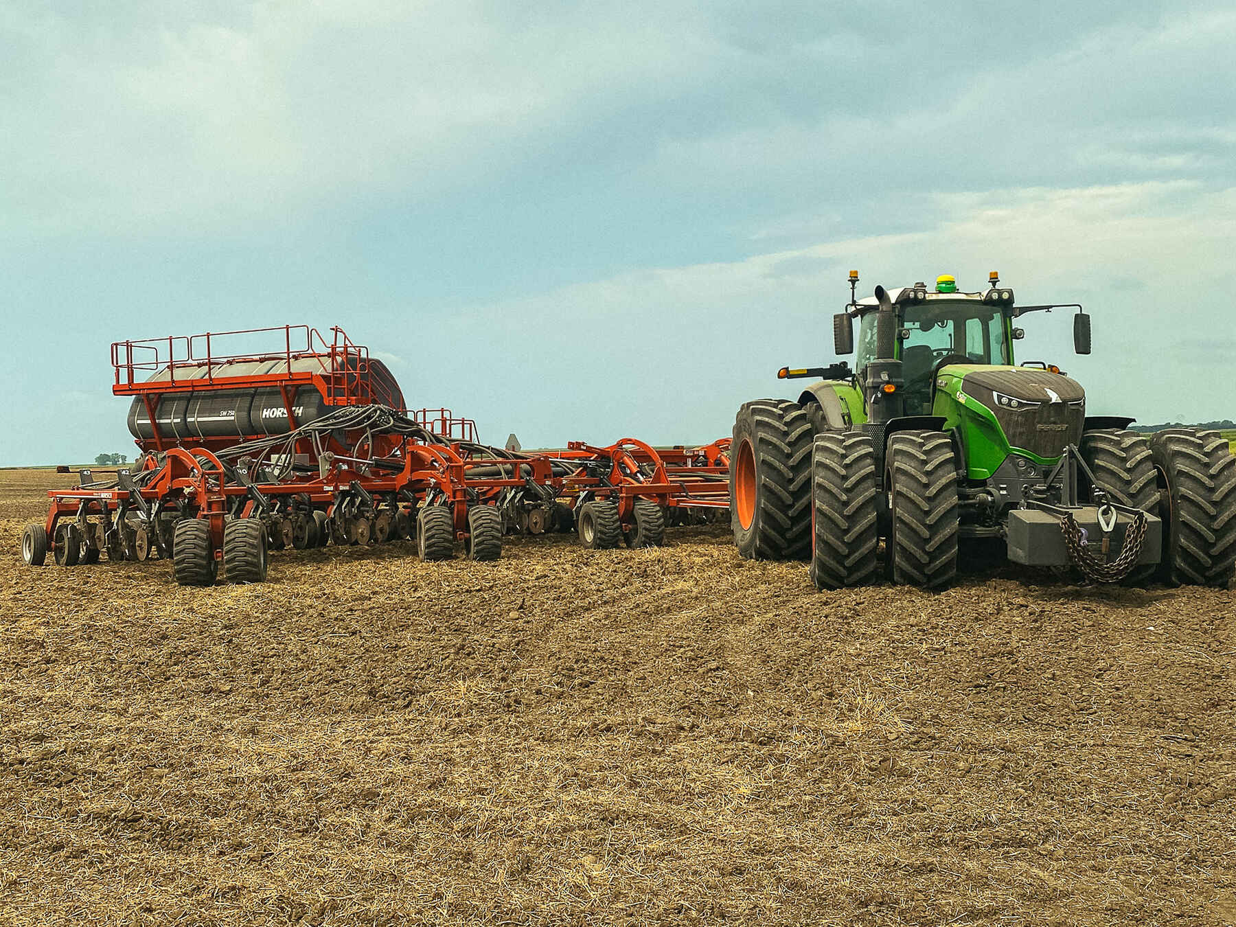Green tractor pulling red agricultural planting equipment across a freshly tilled field