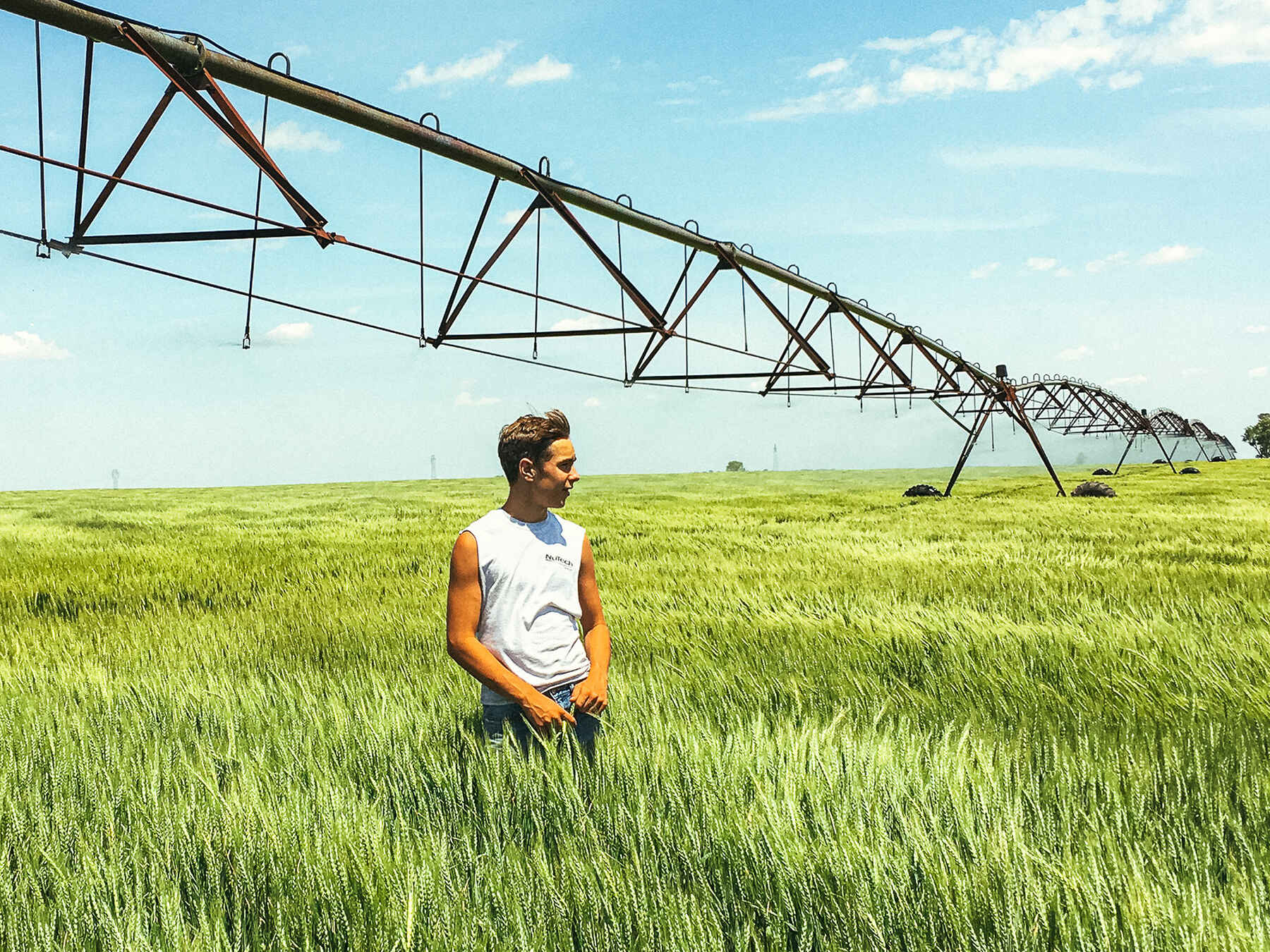Young farmer standing in a green grain field beneath a center pivot irrigation system