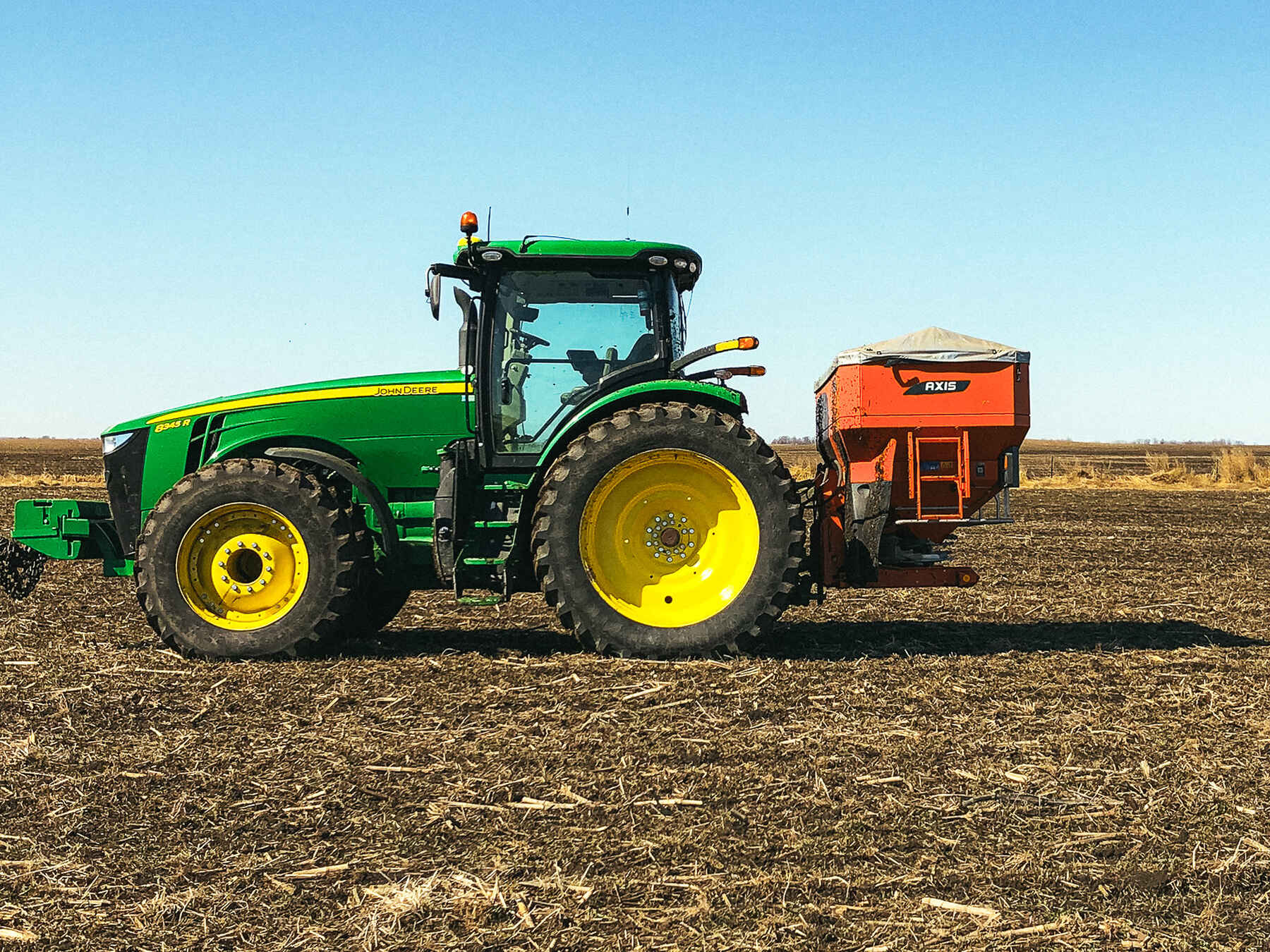 John Deere tractor with yellow wheels towing an orange grain cart across a harvested agricultural field