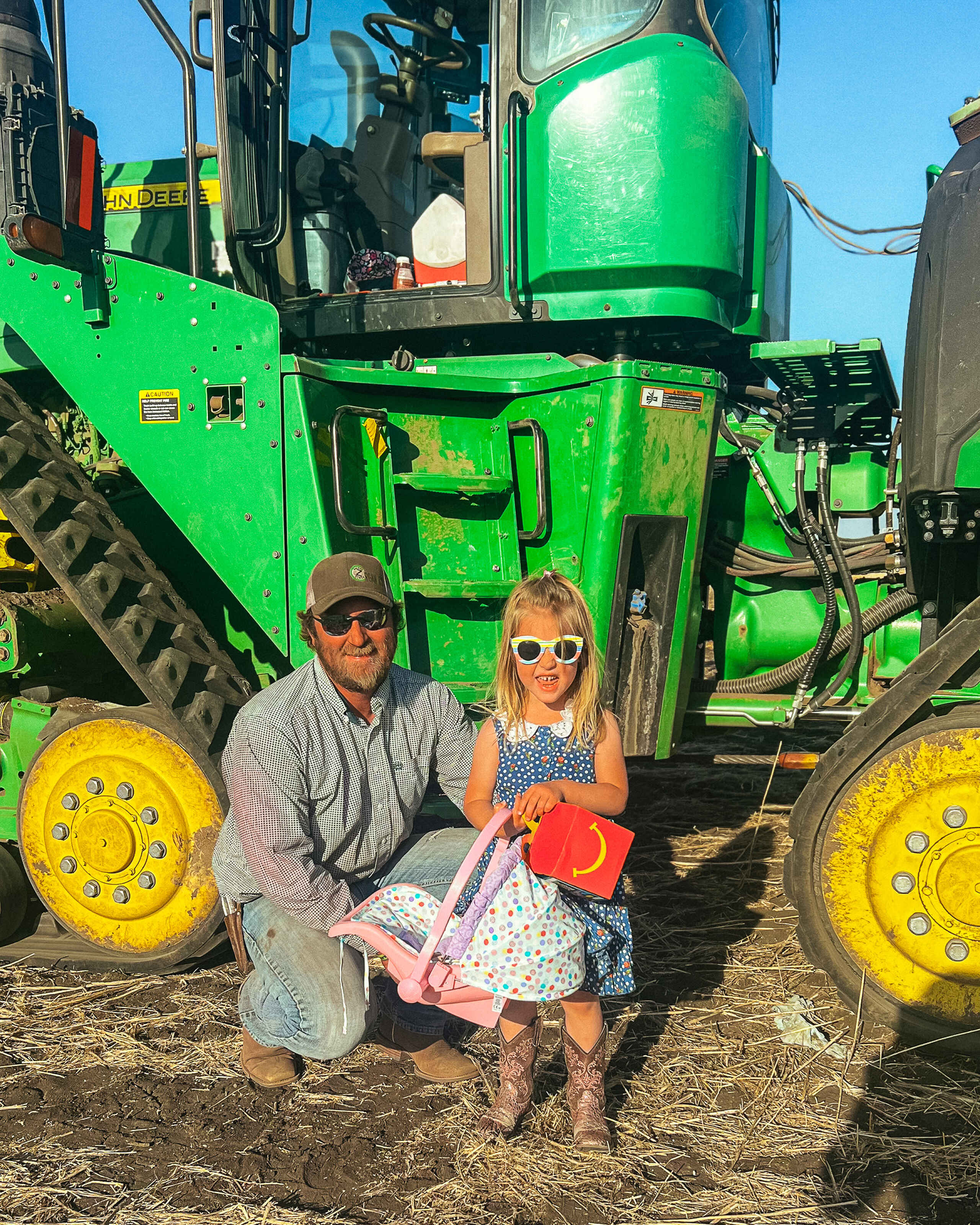 Man and young girl posing in front of a green John Deere tractor with yellow wheels