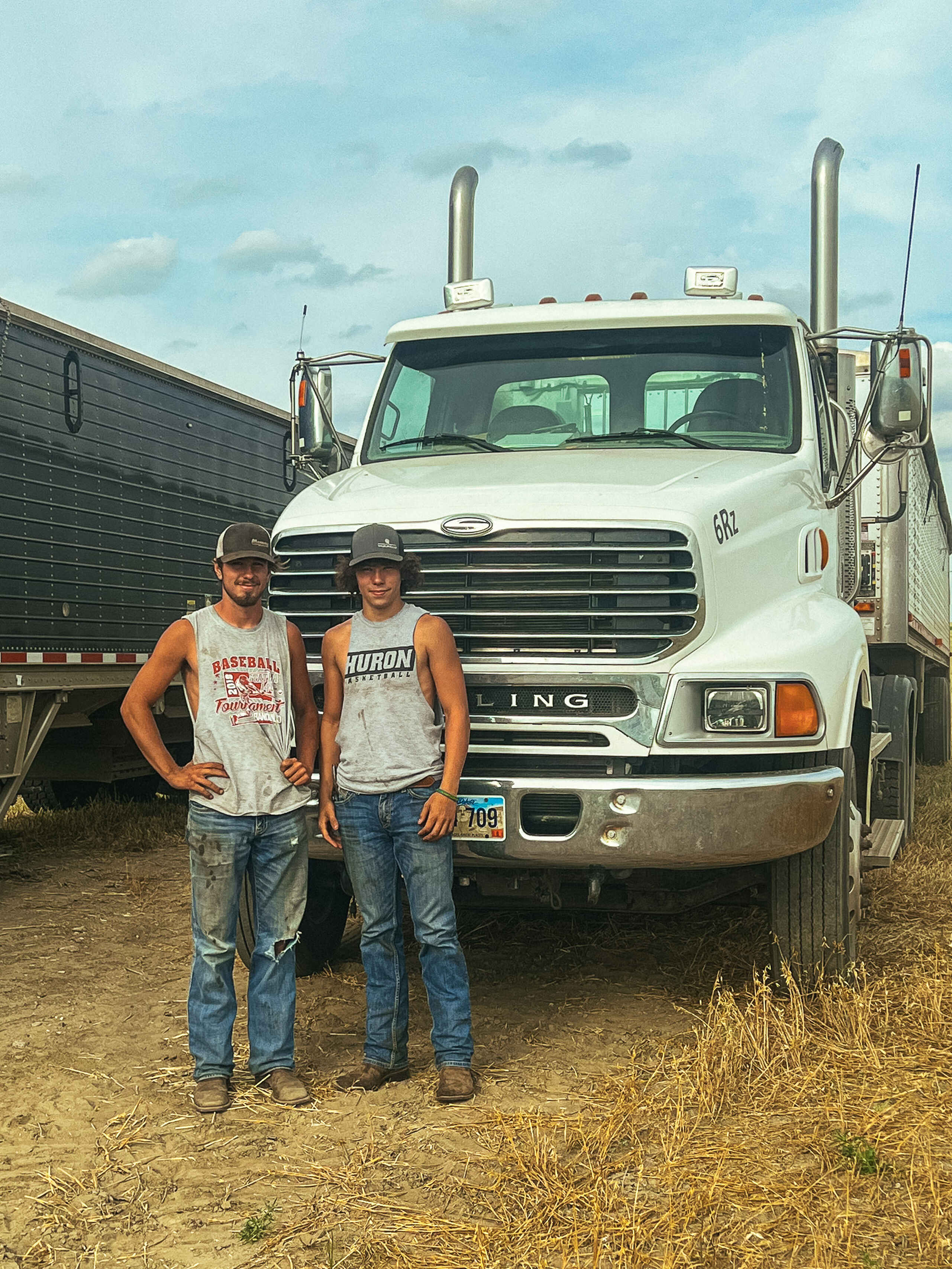 Two men stand in front of a white Sterling semi truck on their farm